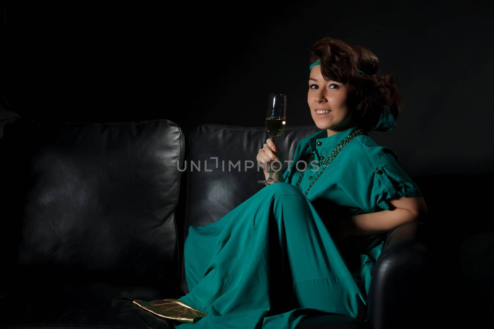 Beautiful girl sitting on a sofa with glass of wine, black background
