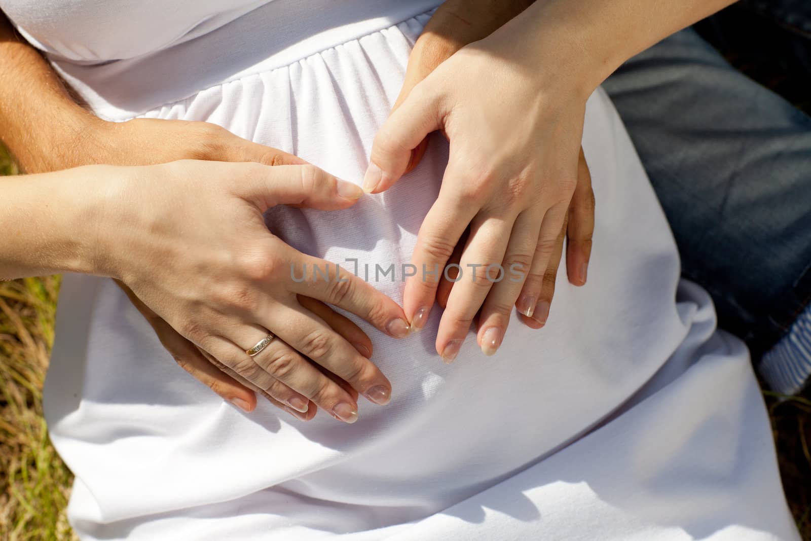 hands of man and girl making heart with hands on the belly ot the pregnant woman