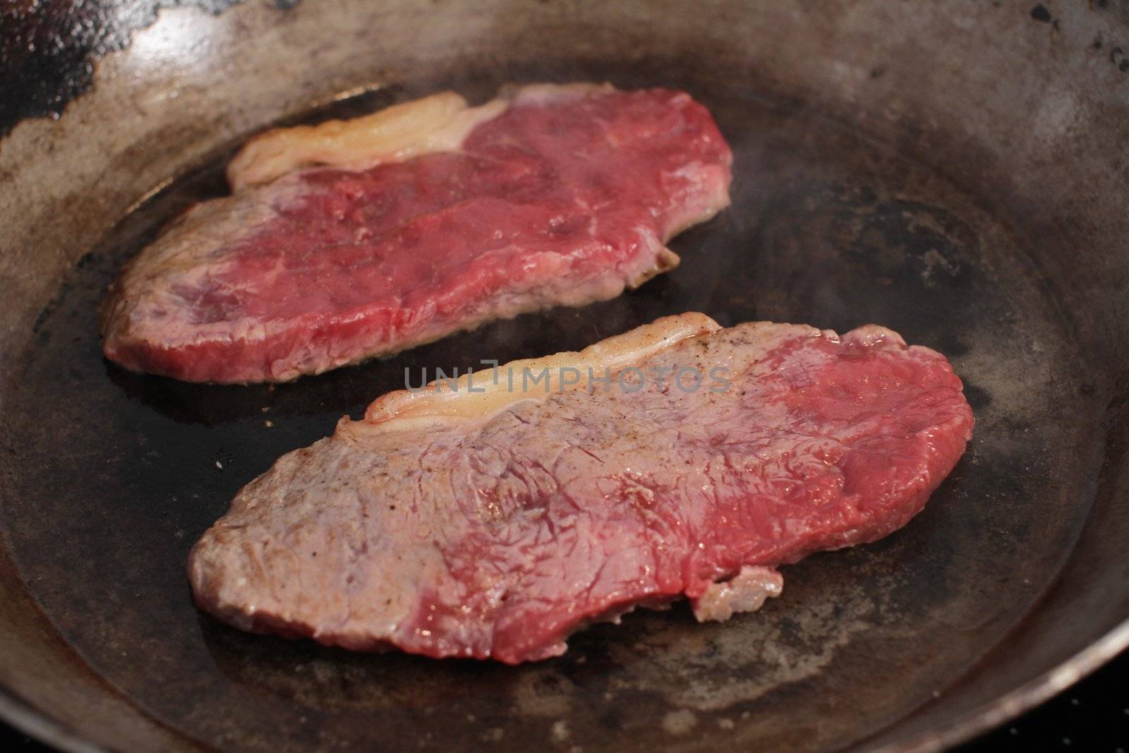 Beef steak cooking in a iron grill pan.