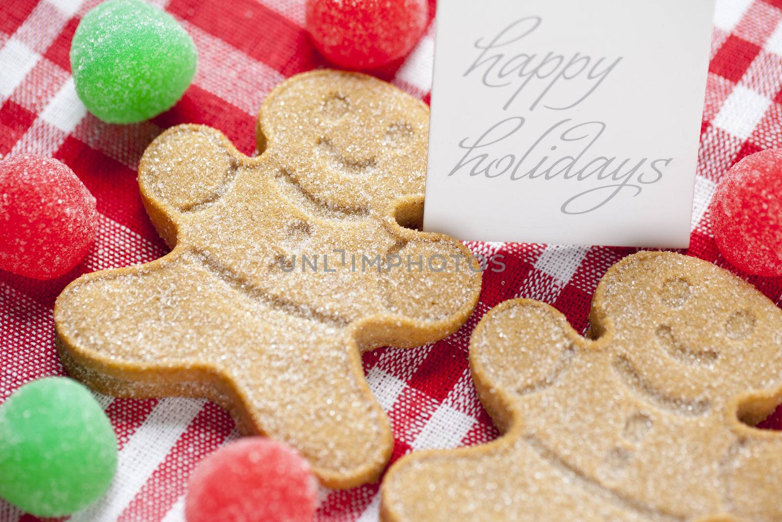 Close-up cropped image of gingerbread candies with happy holidays tag over red checked napkin.