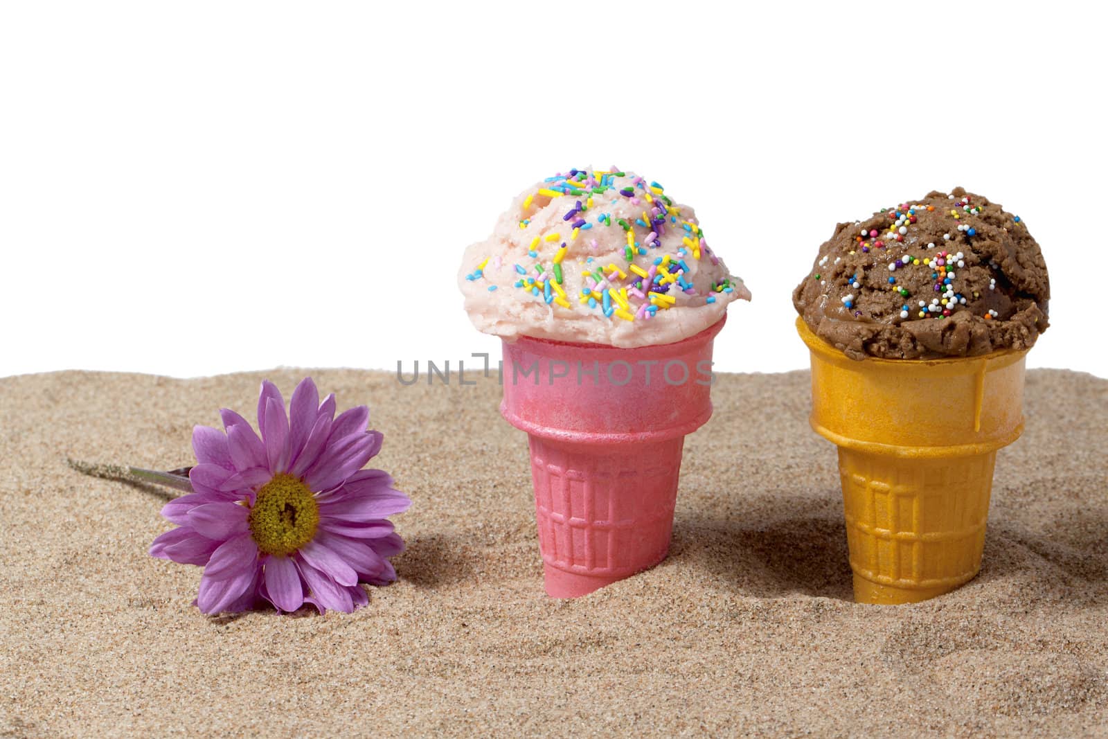 Cone of strawberry and chocolate ice cream in beside a daisy flower laid in beach sand over white background