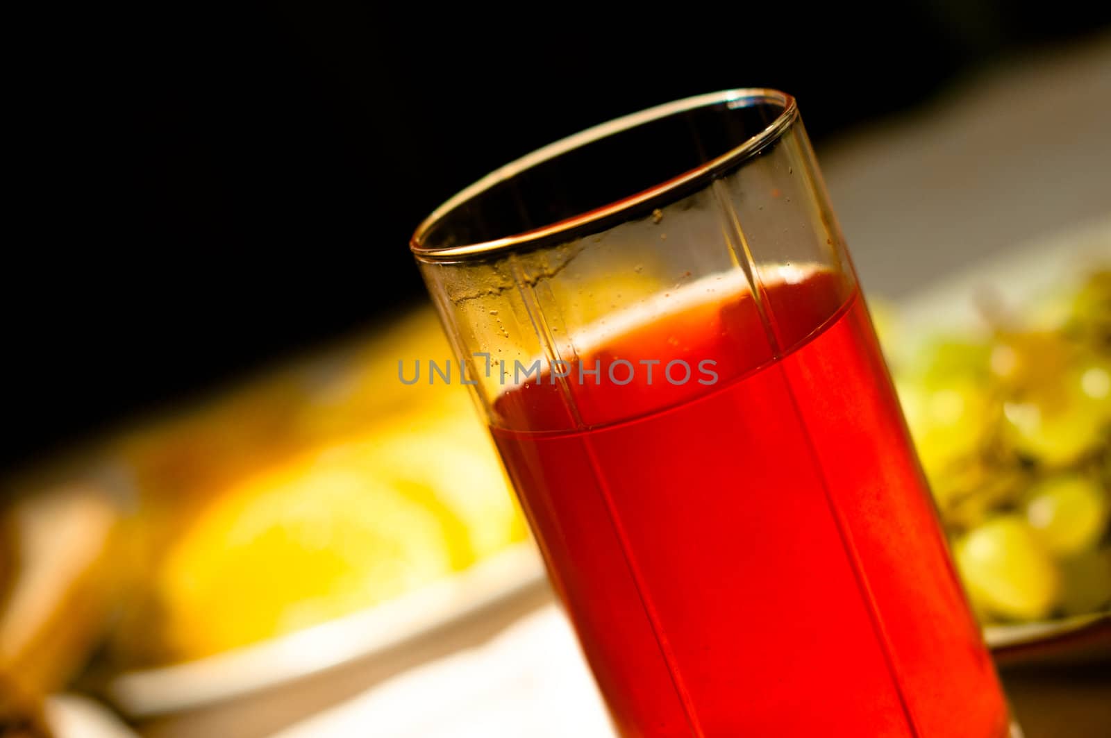 Red fruit-drink in glass in still life composition with orange and grape