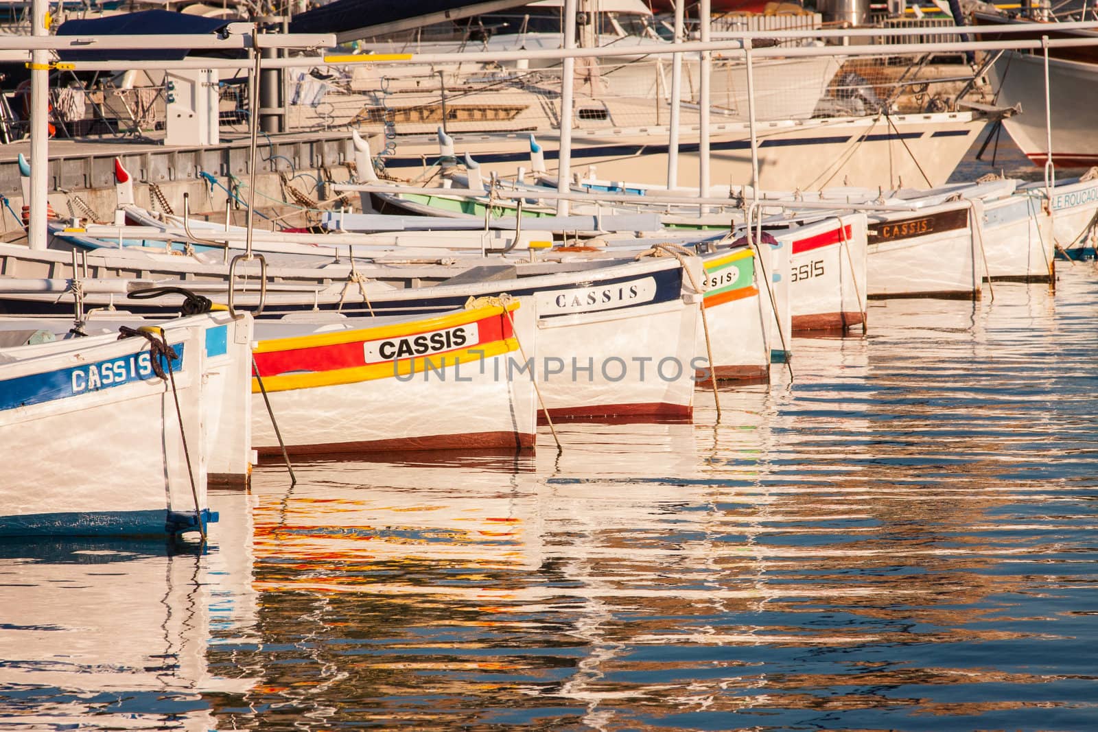 Row of colourful boats in the port which have Cassis painted on their side, and reflection can be seen on the water