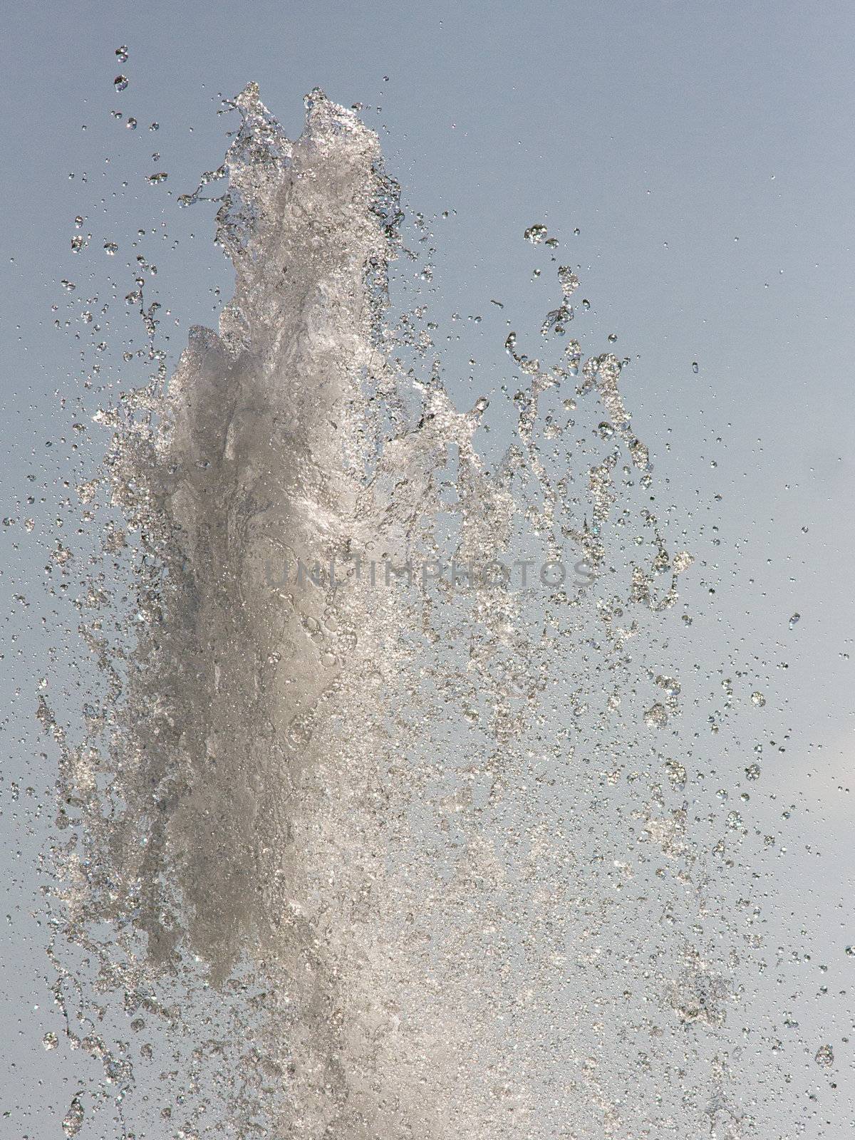 Close up photo of water splashing up the air with waterdrops around and the blue sky in the background