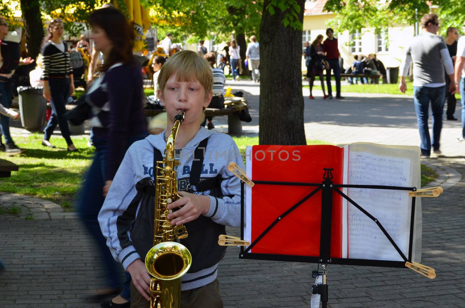 VILNIUS, LITHUANIA - MAY 2012 - Unidentified child play saxophone. People walk around. Street Musician Day.