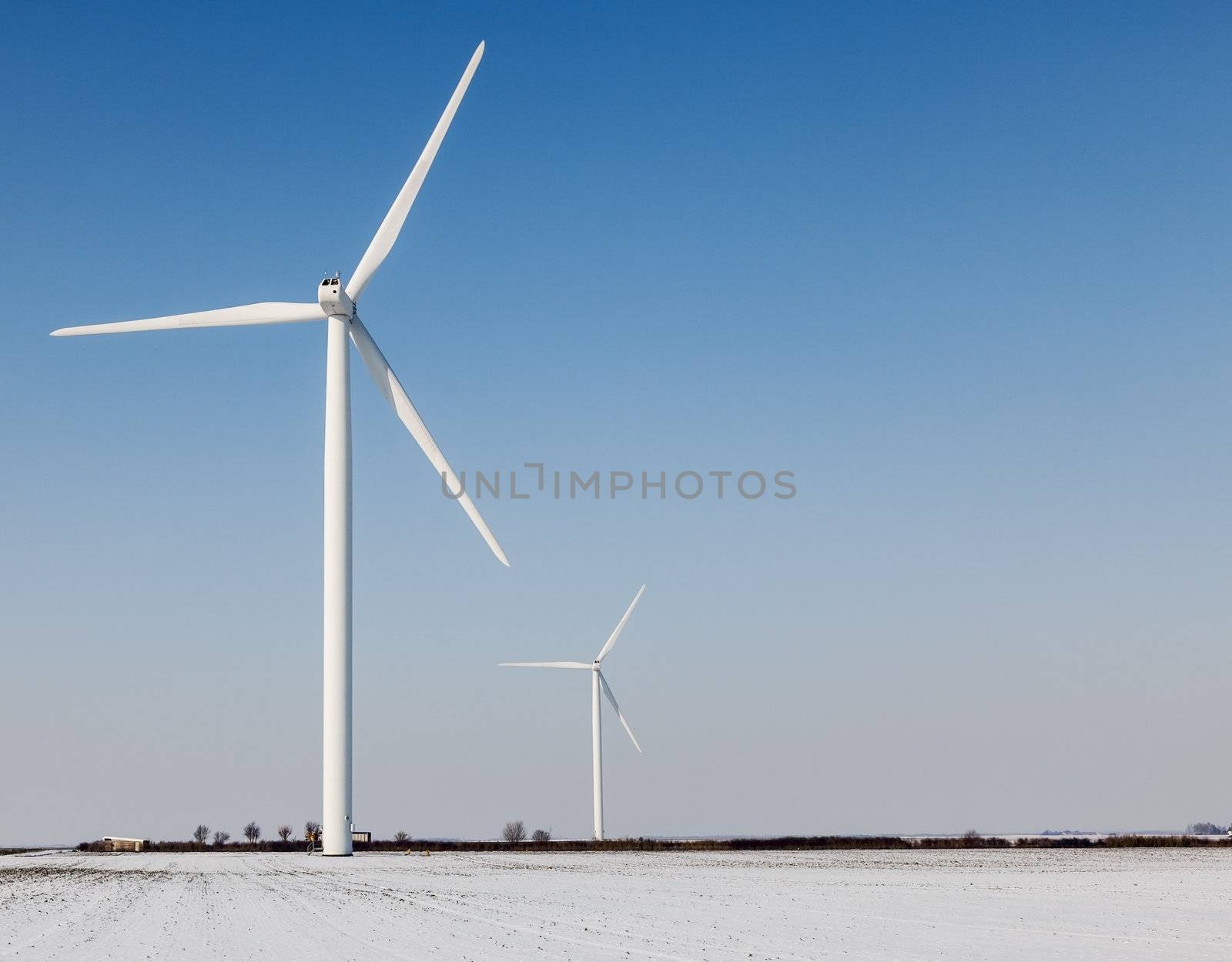 Two windturbines on a field covered by snow in winter.