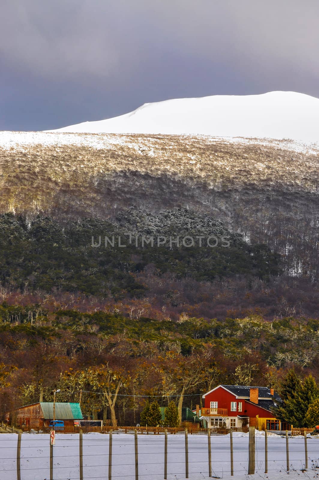 A farmhouse with a snowy hill and forest behind it.