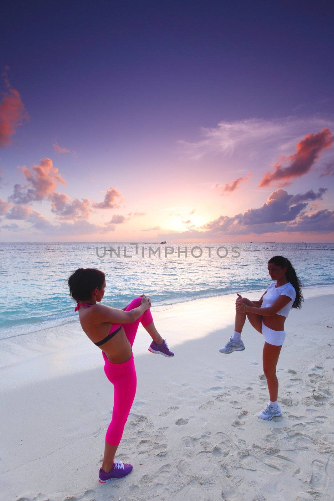 Sport fitness women stretching on sunset beach near sea