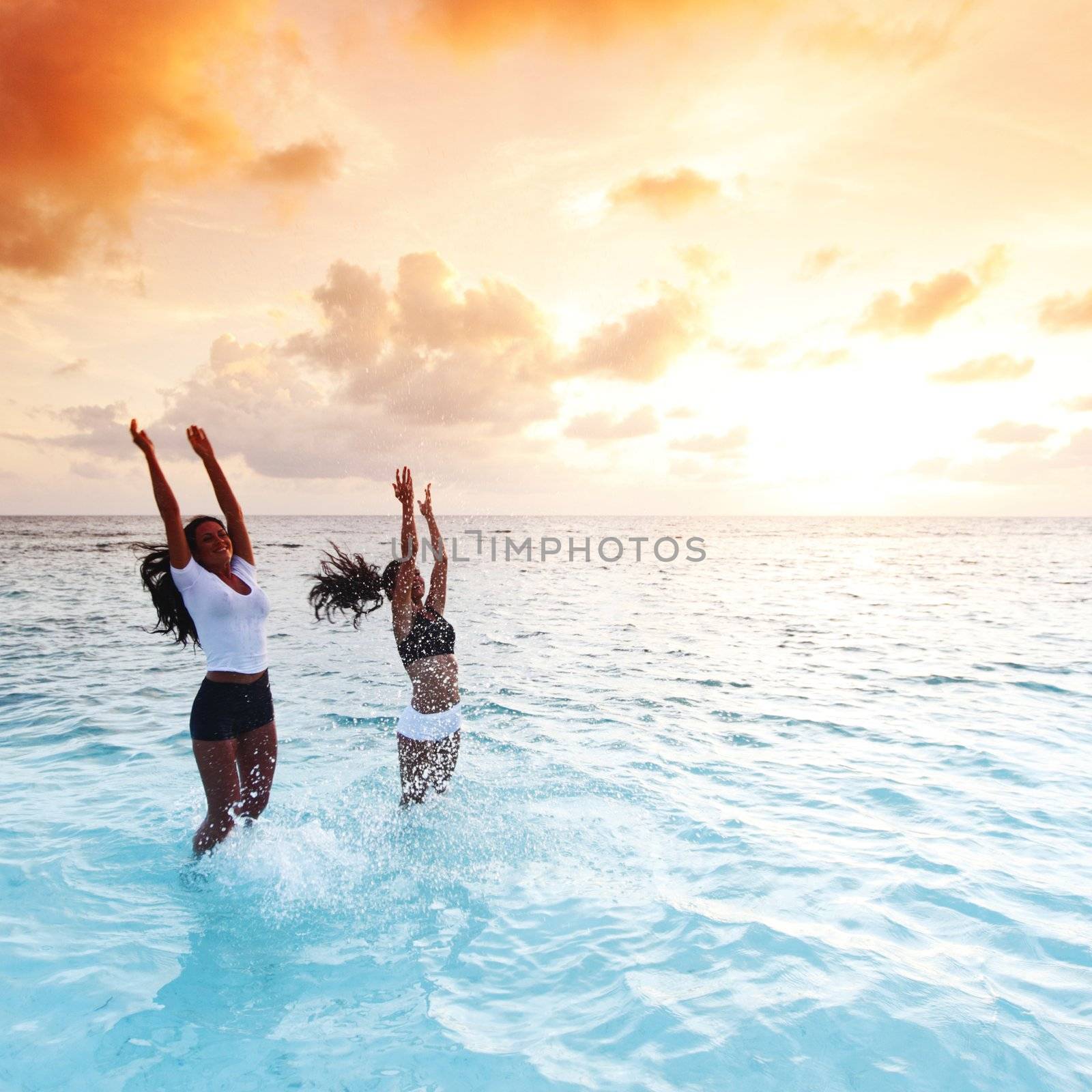 Two happy wimen playing in water on sunset