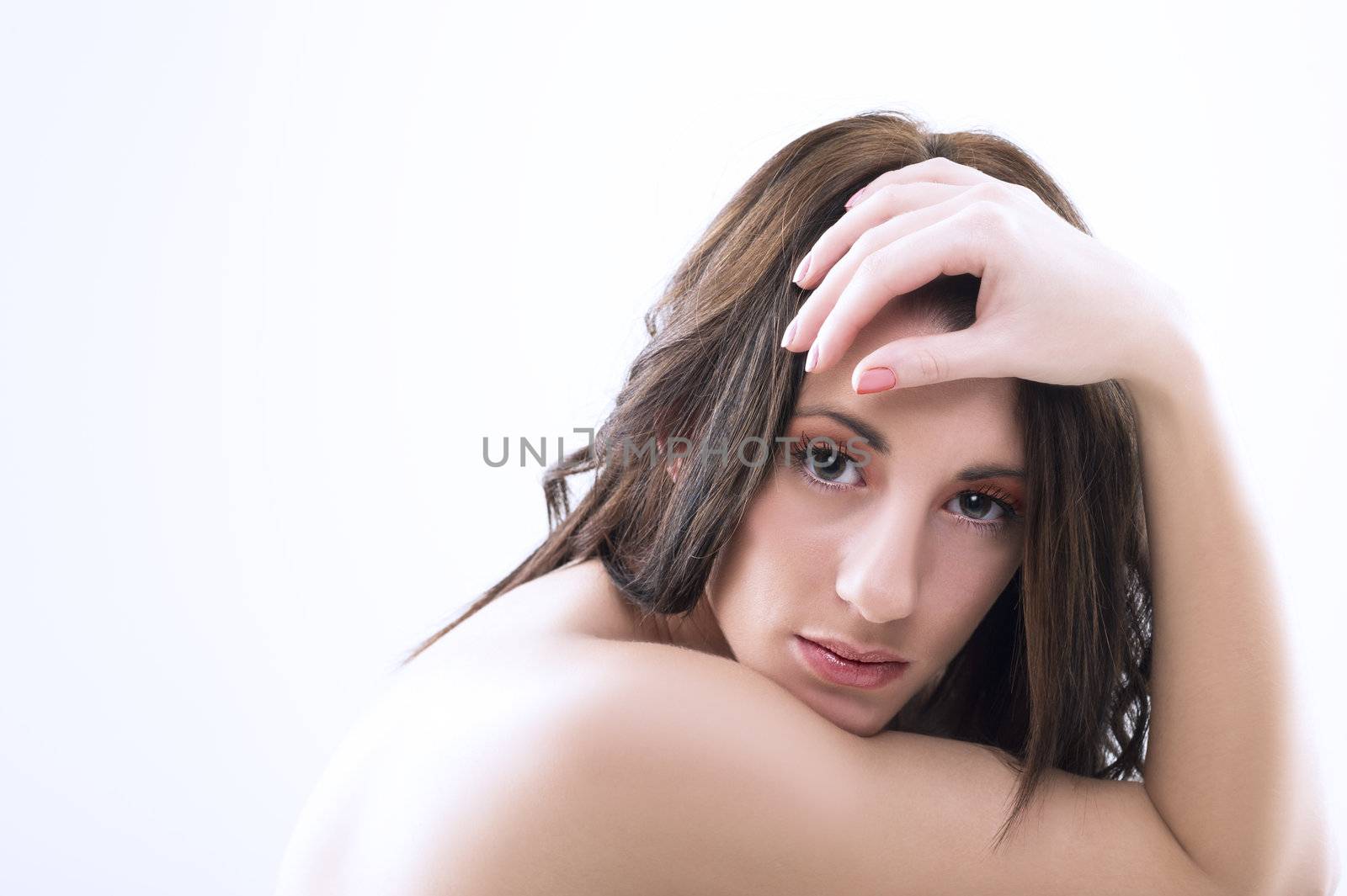 Serious pensive attractive woman with bare shoulders and tousled long brunette hair looking directly at the camera in studio