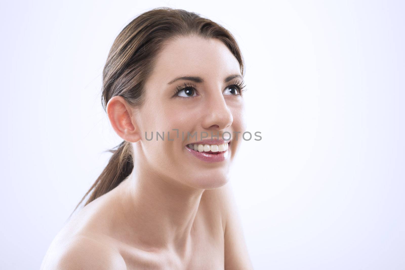 Head and shoulders portrait of a beautiful sexy woman with lovely smile and bare shoulers looking upwards with her eyes raised.