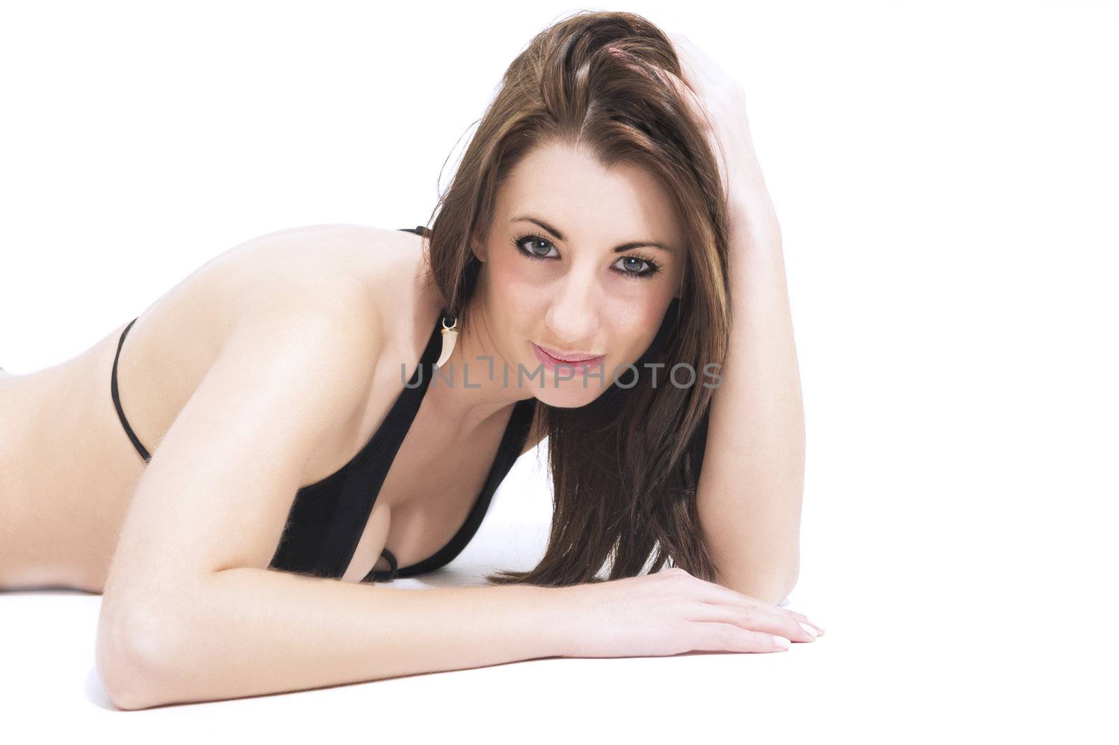 Seductive beautiful woman in a bikini lying on a white studio background on her stomach looking at the camera with a sultry look
