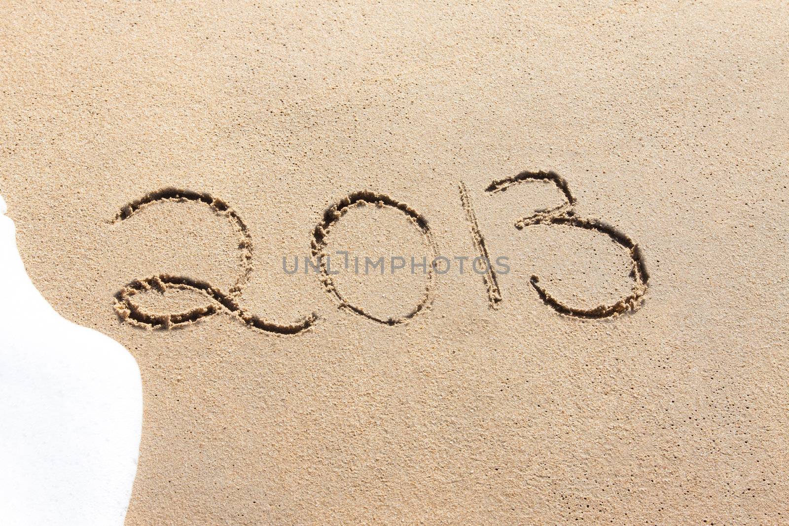 2013 written in the sand on a beach with foamy water about to wash it away.