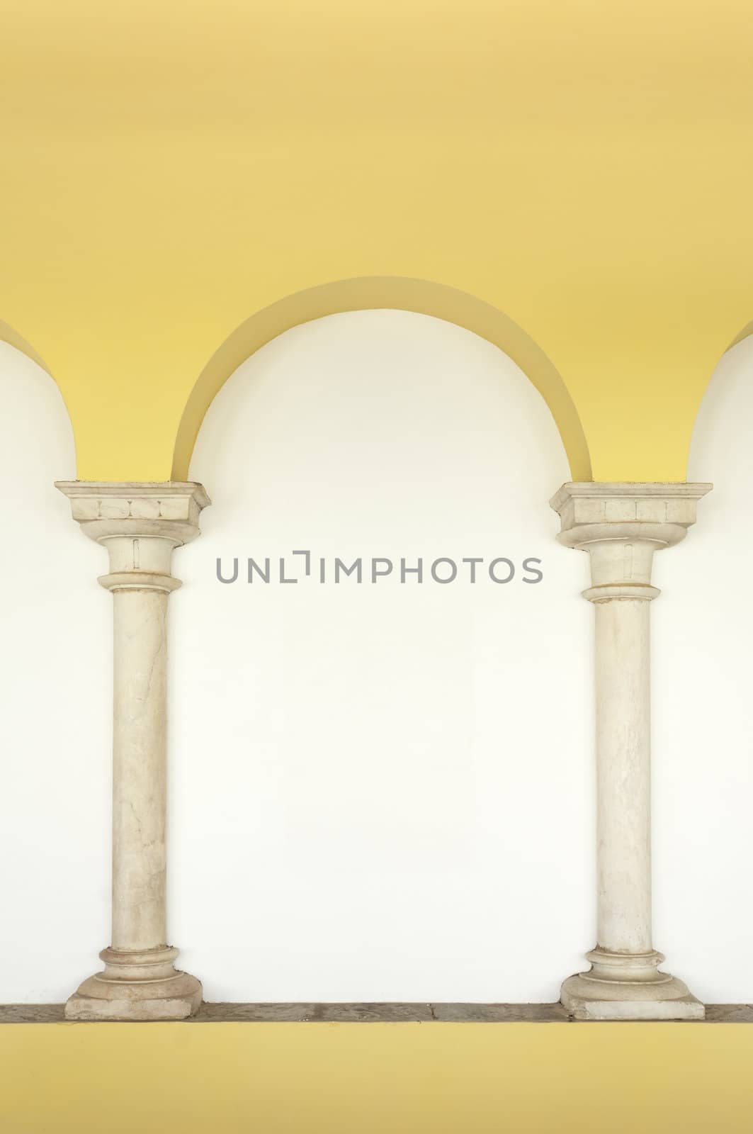 Two marble columns embedded in the wall topped by an arch painted in yellow, Elvas, Portugal