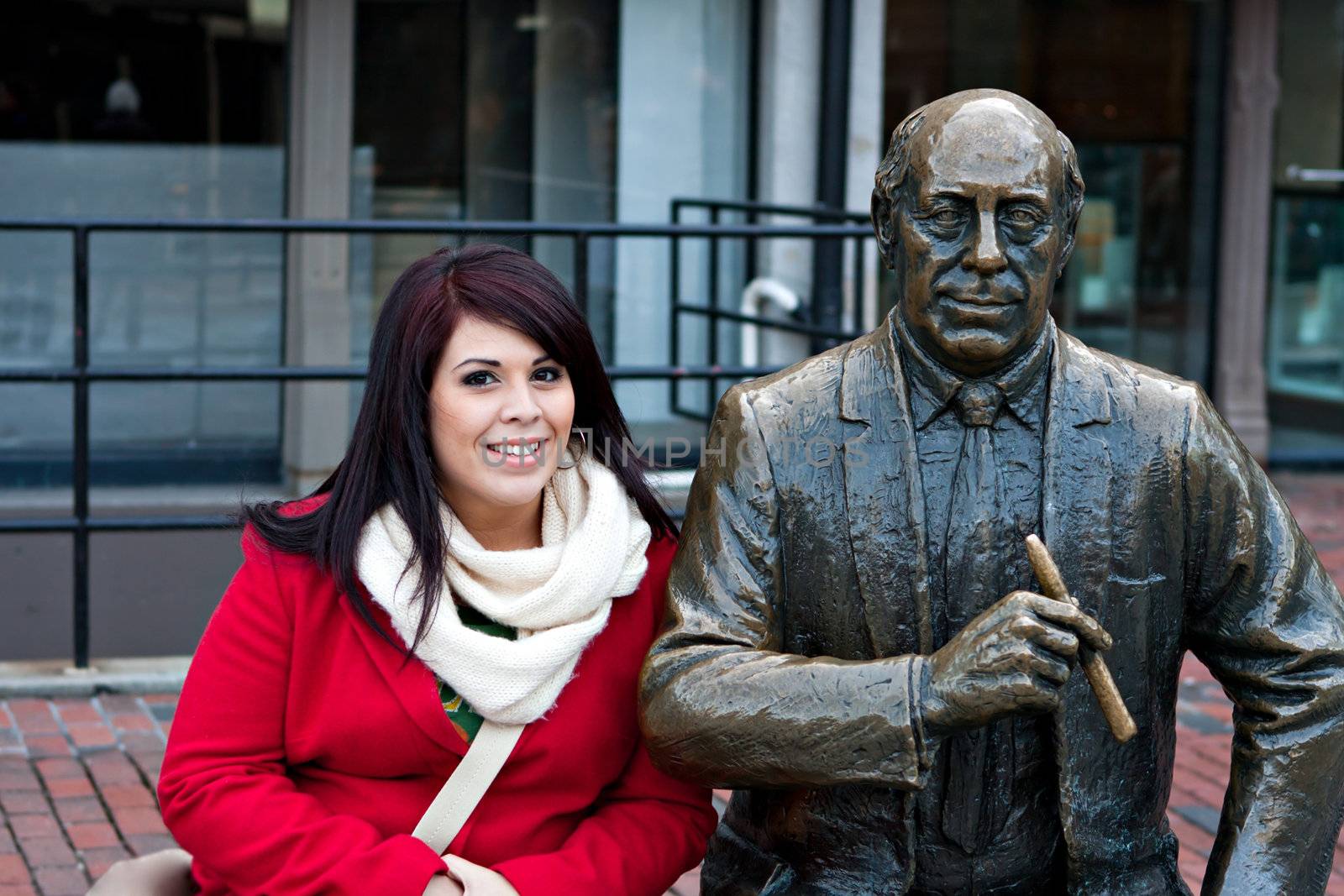 Young woman puts her arm around the public Red Auerbach statue found in Bostons Quincy Market just outside of Faneuil Hall.