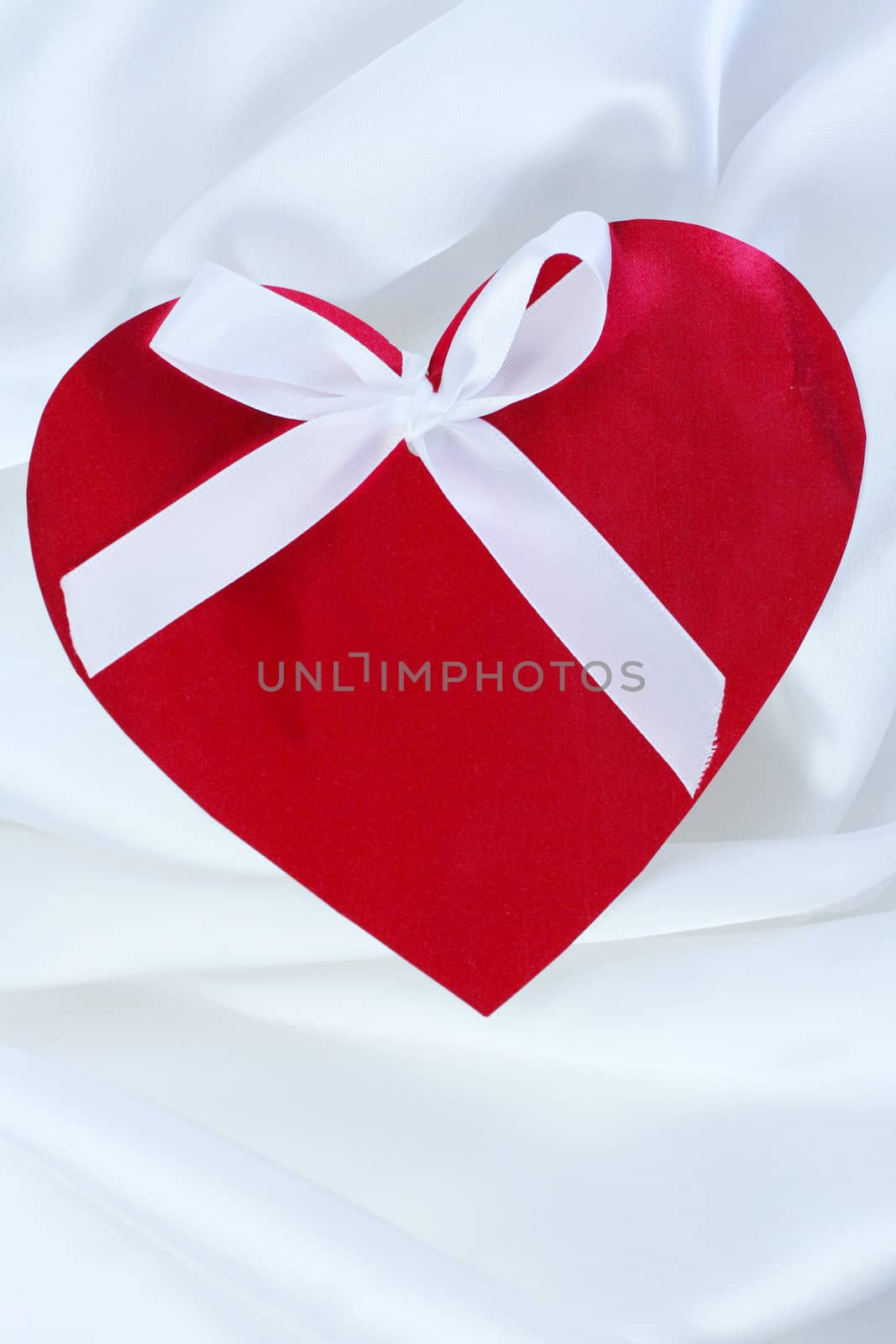 Red heart with ribbon on white satin