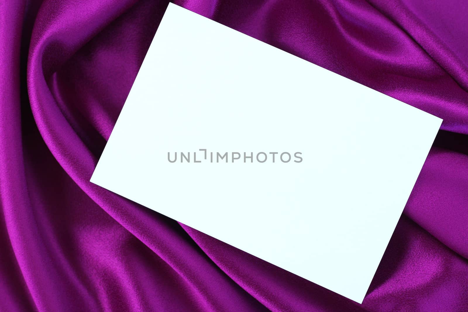 Blank white card on purple and magenta colored satin cloth.
