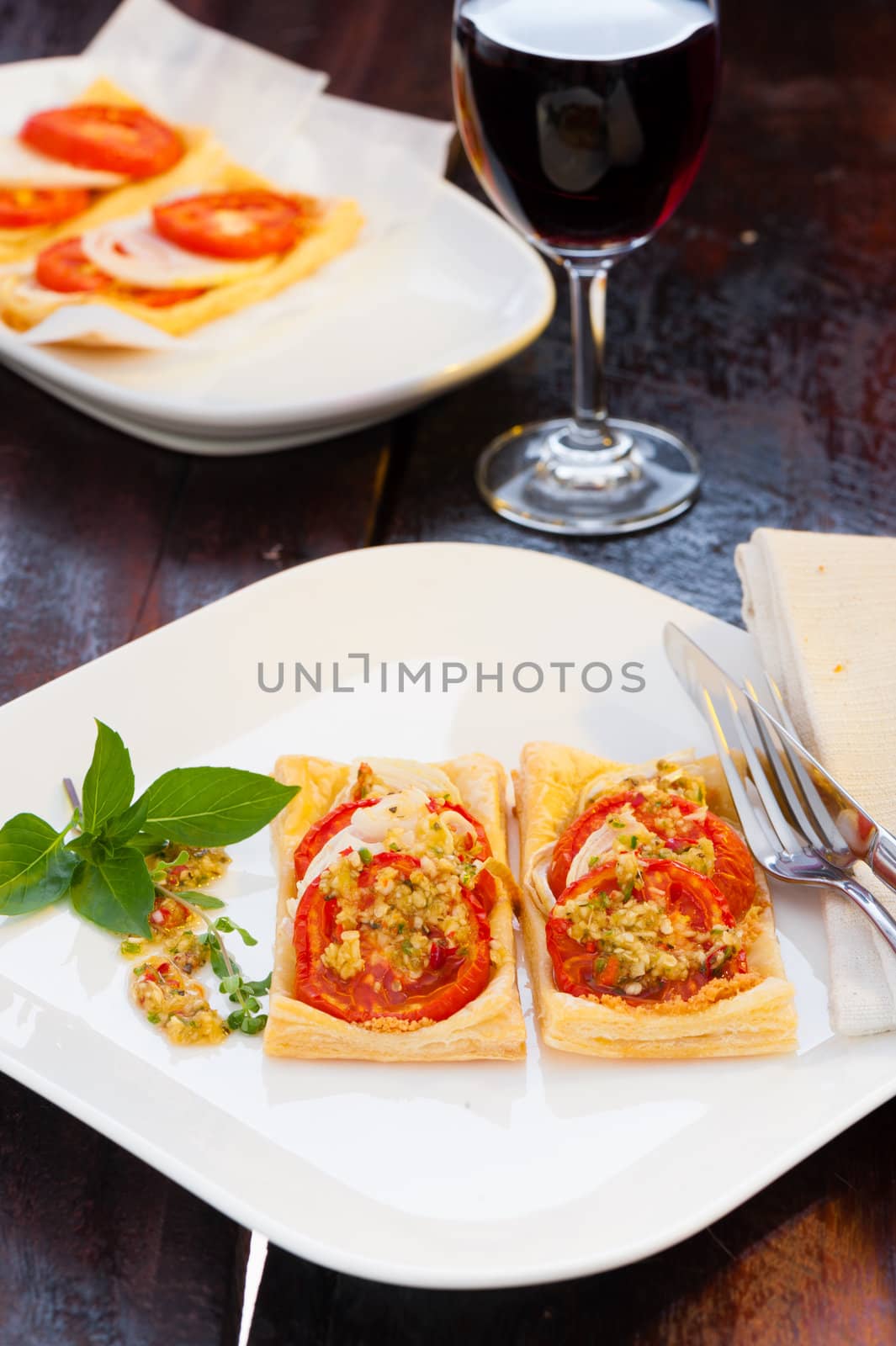 Two small piece of mini pizza with some herbs on white plate and a glass of red wine in the background