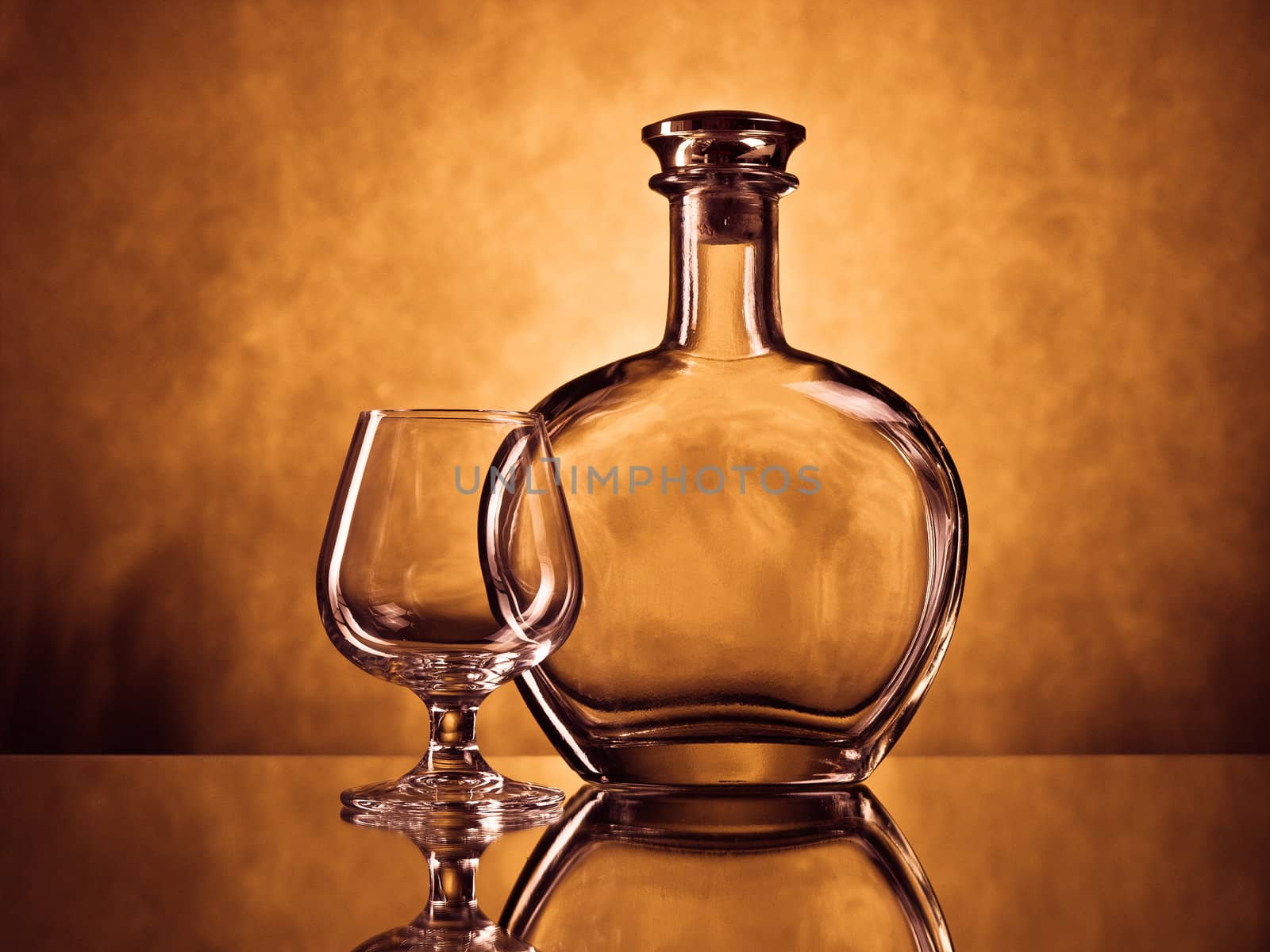 Empty cognac bottle and a cognac glass on a reflective suface against grunge background