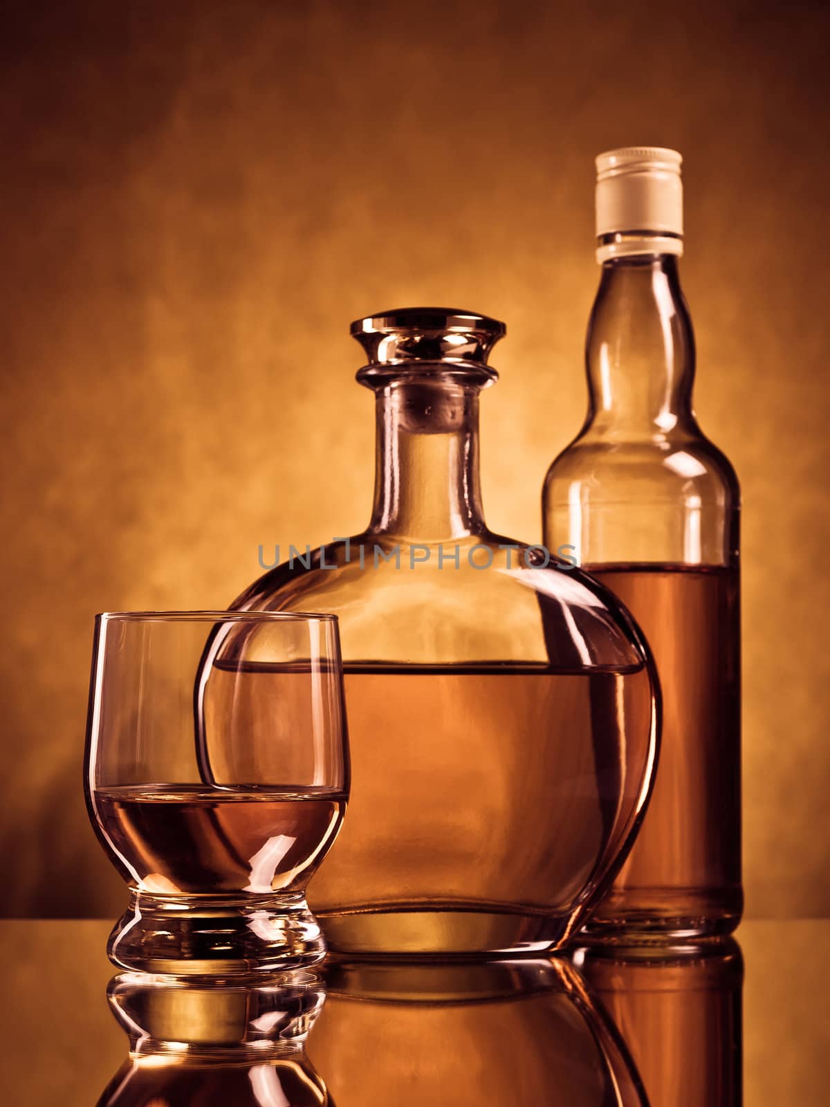 Two bottles of alcohol and a glass on brown grunge background