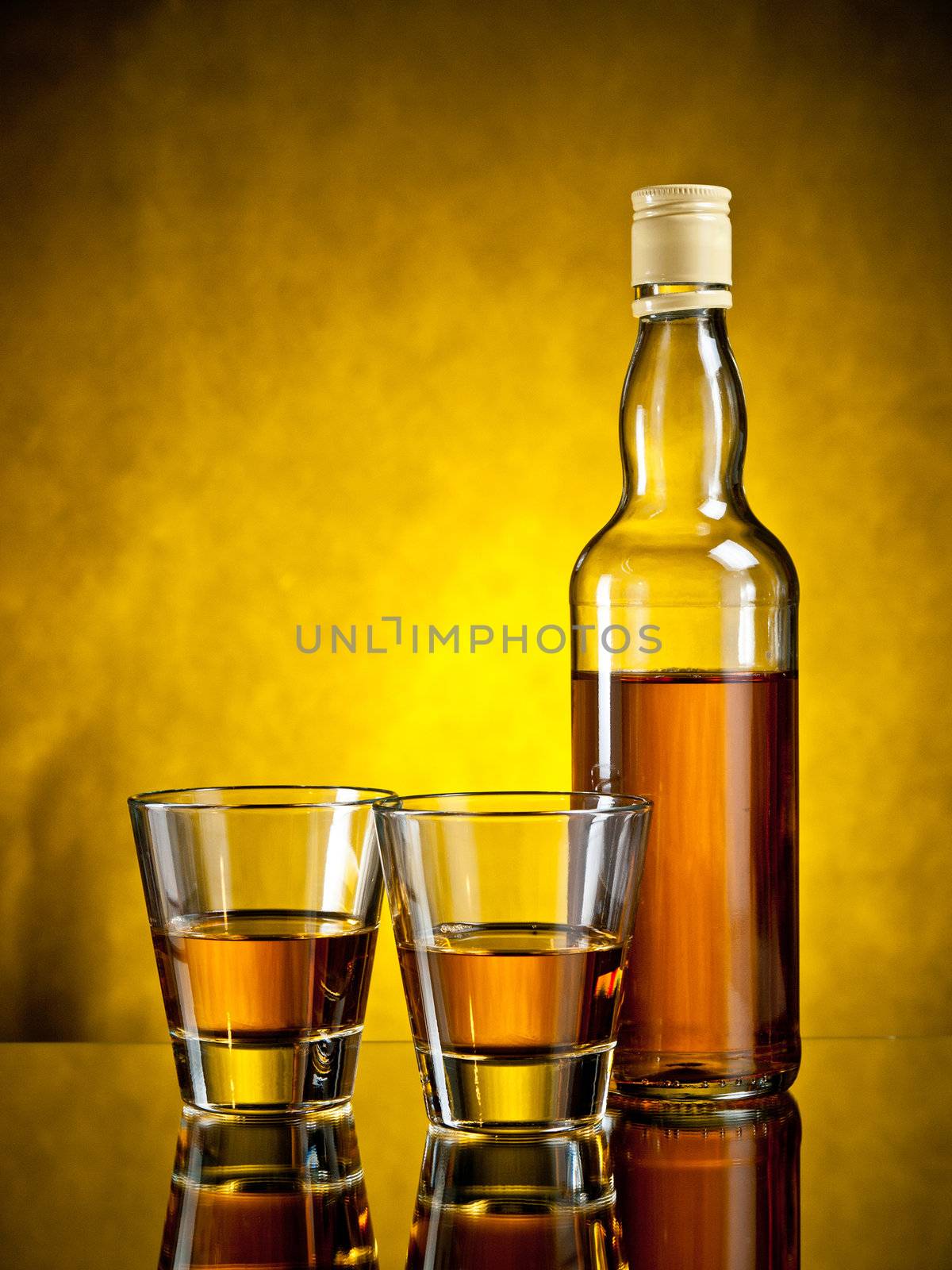 Bottle of whiskey with two filled glasses on yellow grunge background