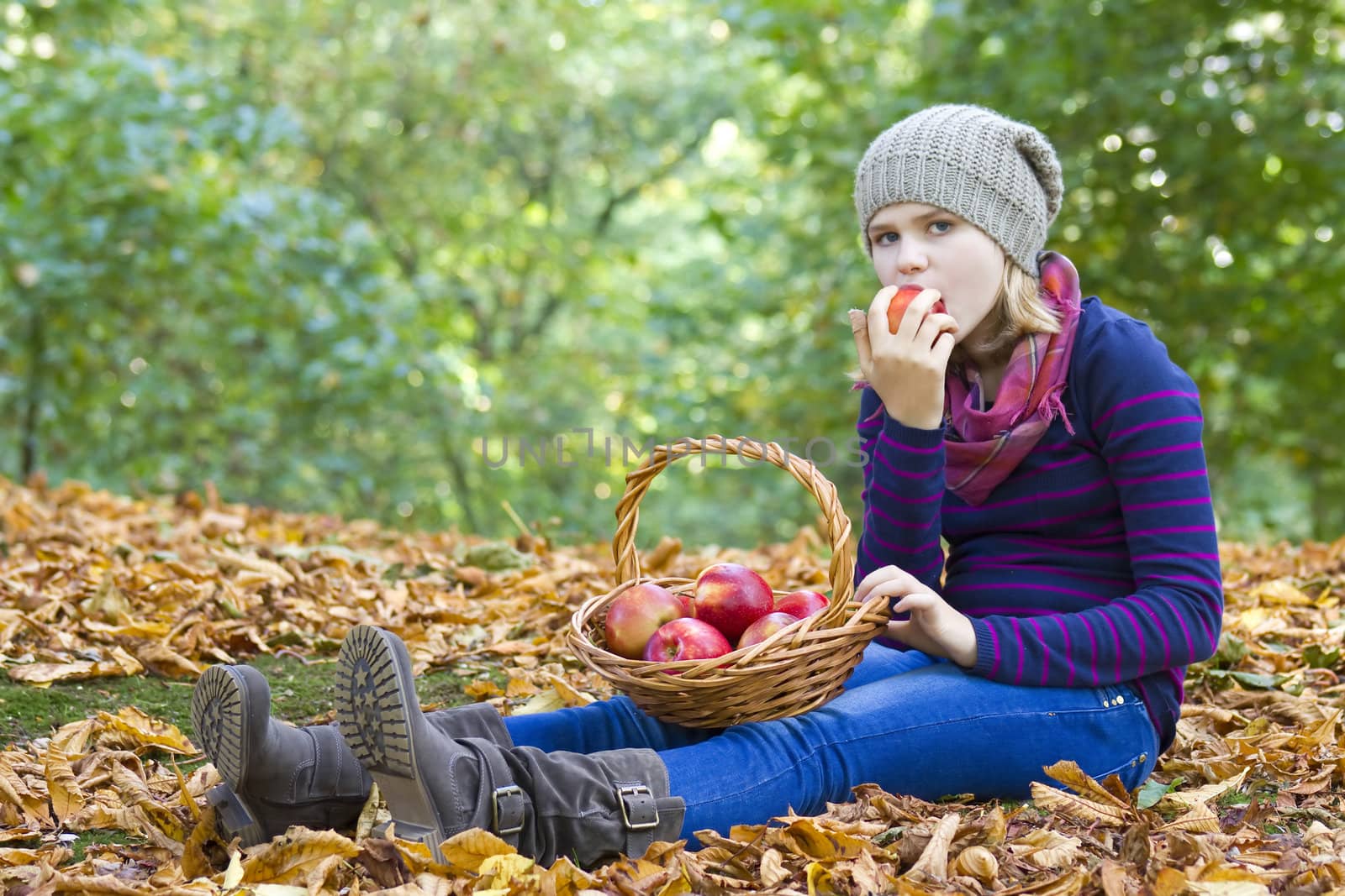 young girl eating red apple in autumn garden by miradrozdowski