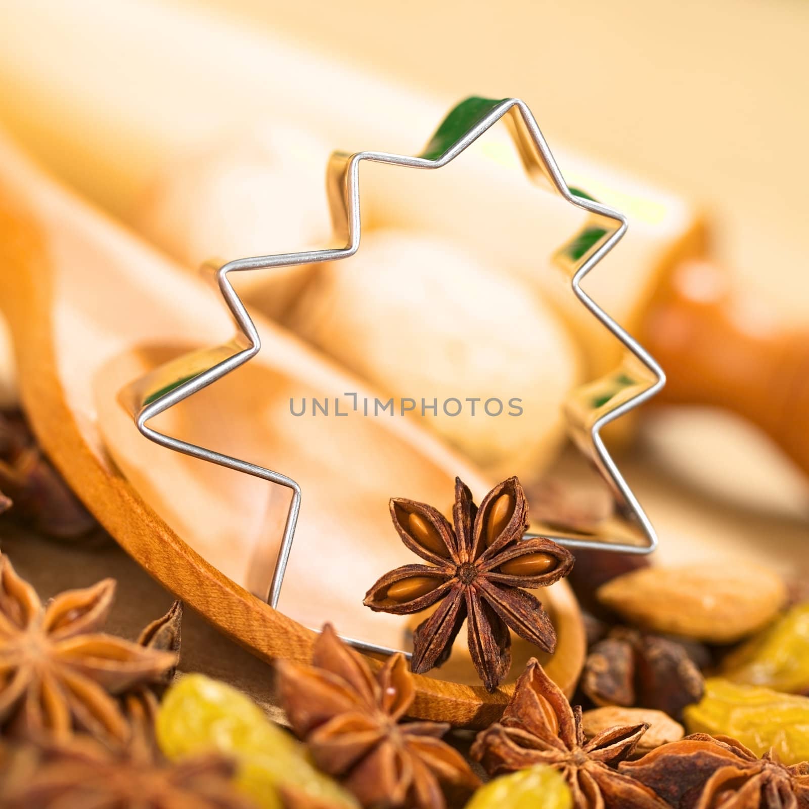 Christmas Baking. Tree shaped cookie cutter with star anise on wooden spoon surrounded by raisins and nuts, with a rolling pin in the back (Selective Focus, Focus on the left side of the cookie cutter and on the anise on the spoon)