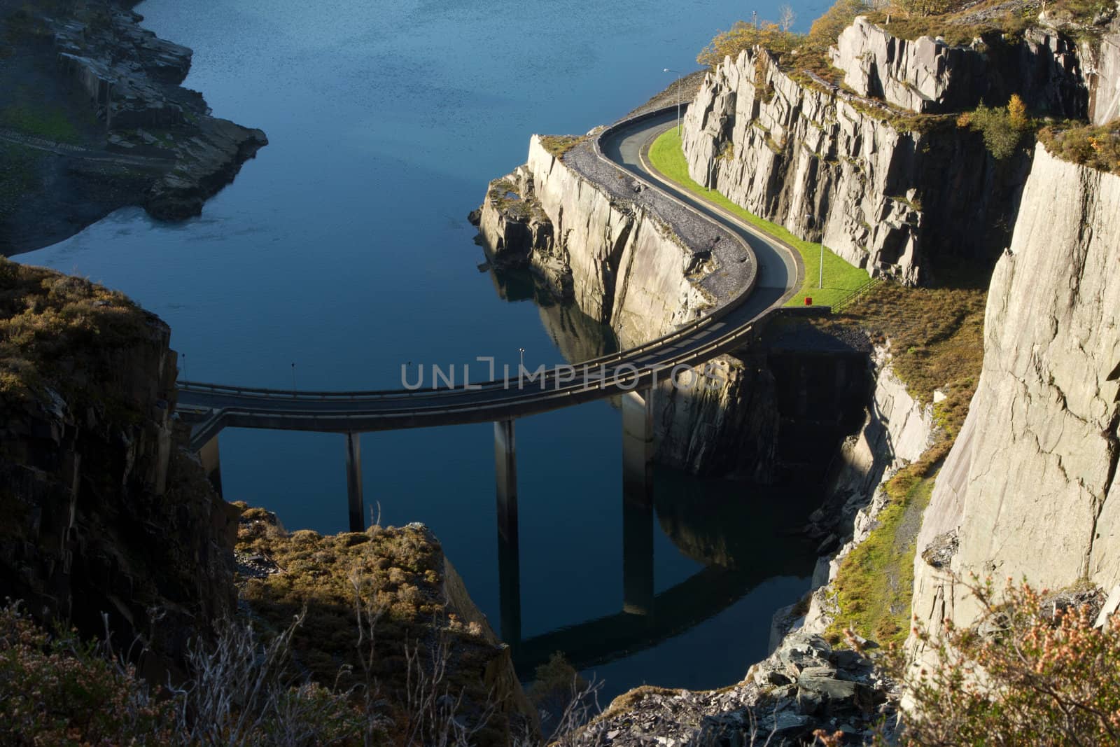 A road bridge on supports curves past cliffs over water.