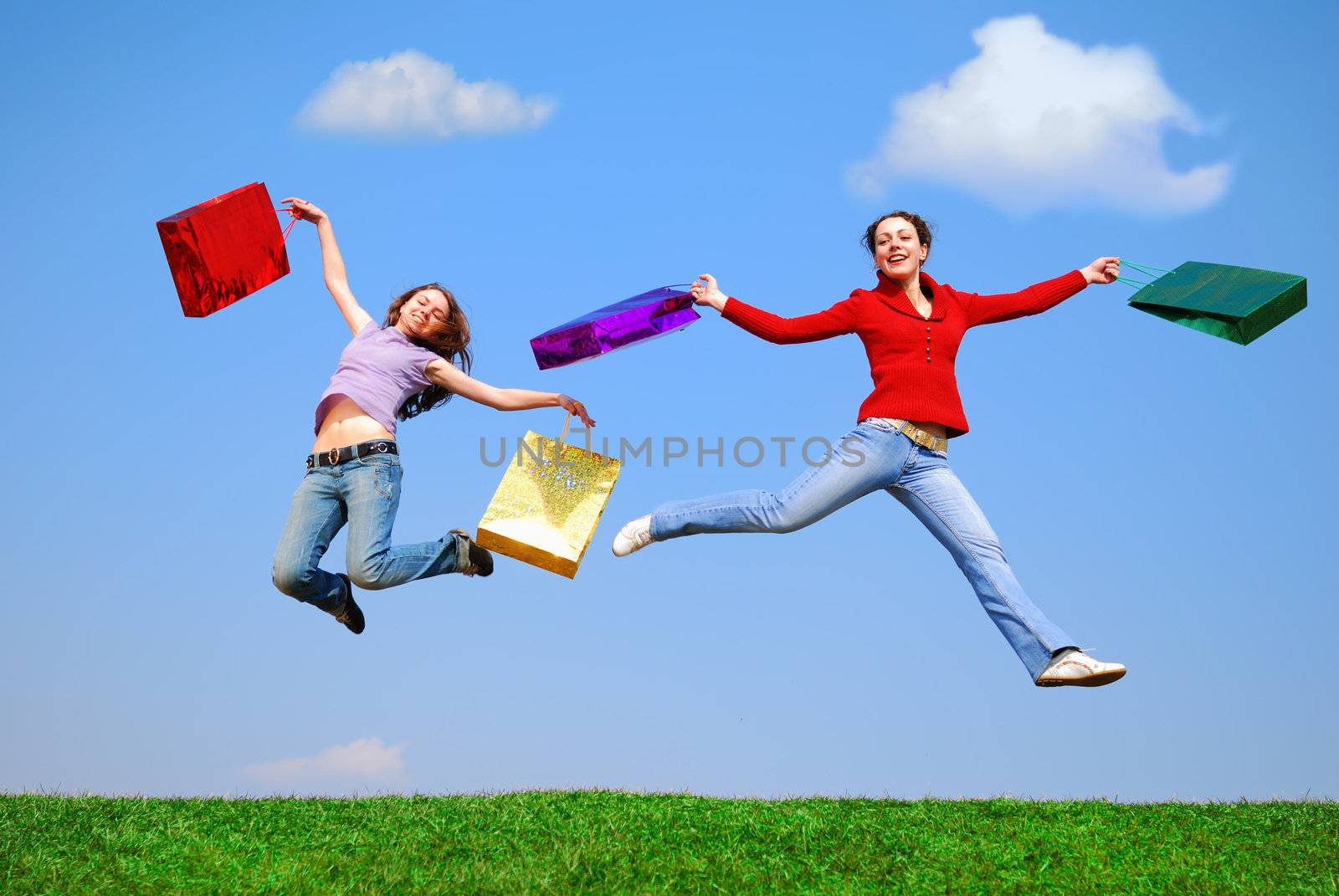 Girls jumping with bags against blue sky