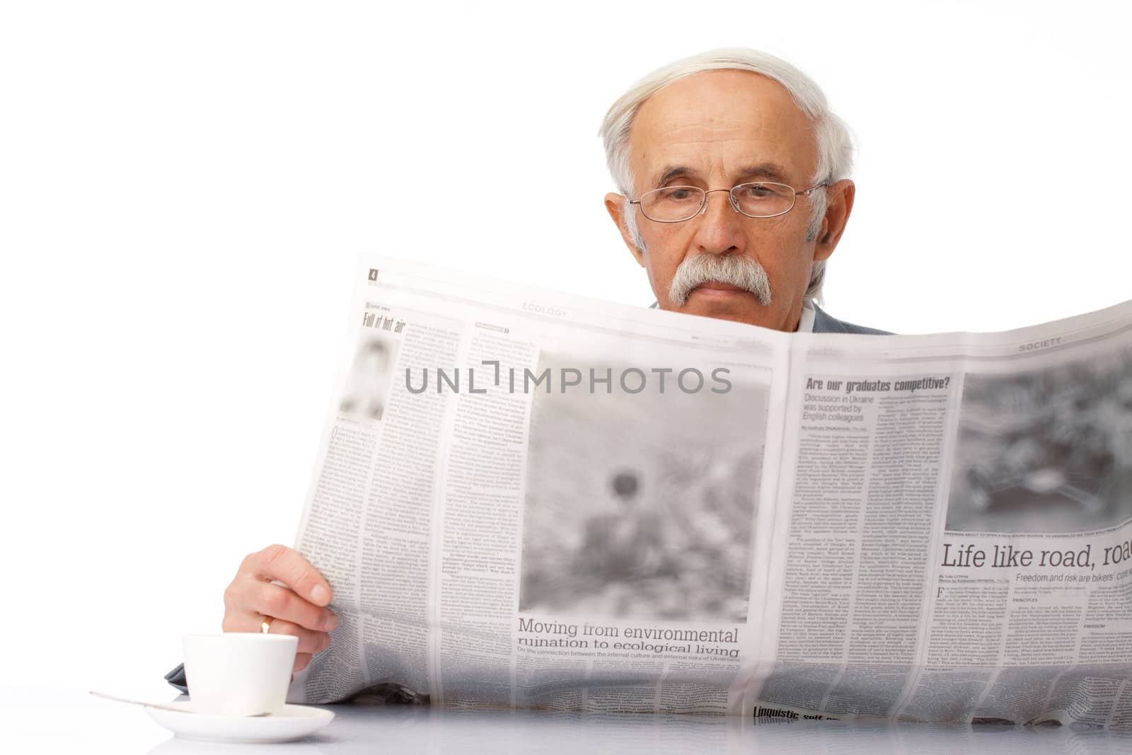 Portrait of an elder businessman reading a newspaper with a cup near him.