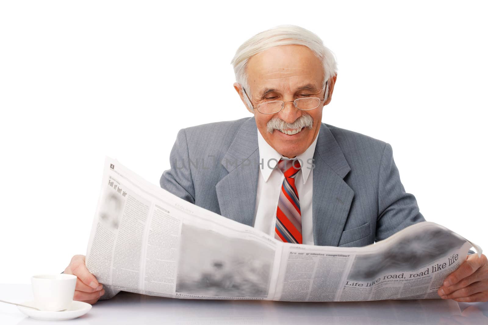 Portrait of an elder happy man reading a newspaper with a cup near him.