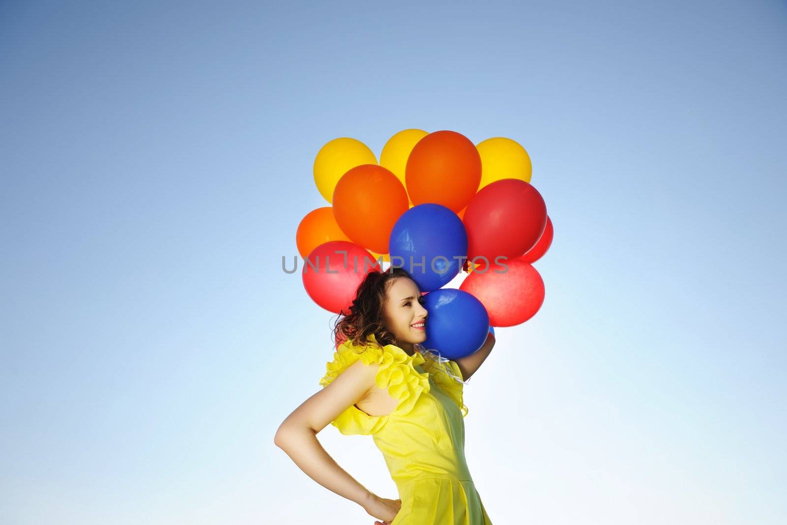 Woman holding balloons against sun and sky