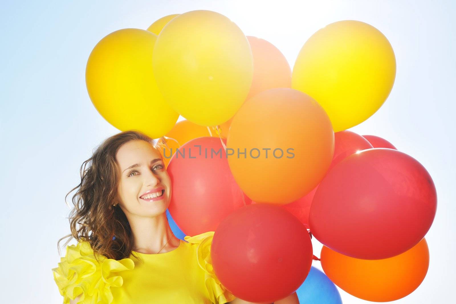 Woman holding balloons against sun and sky