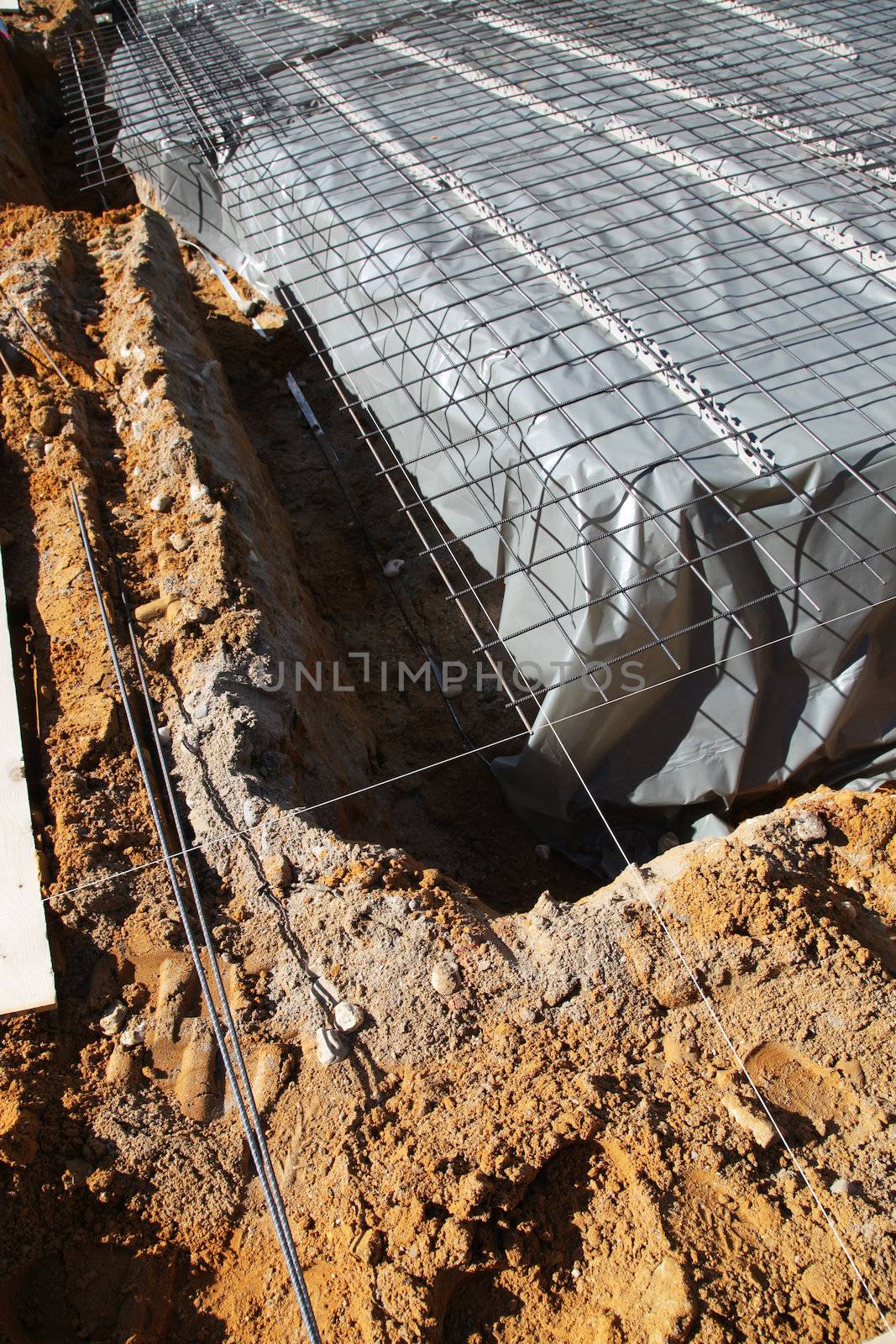 Excavations for the foundations of a new house with the main floor area covered in a sheet of plastic and a mesh of steel reinforcing rods 