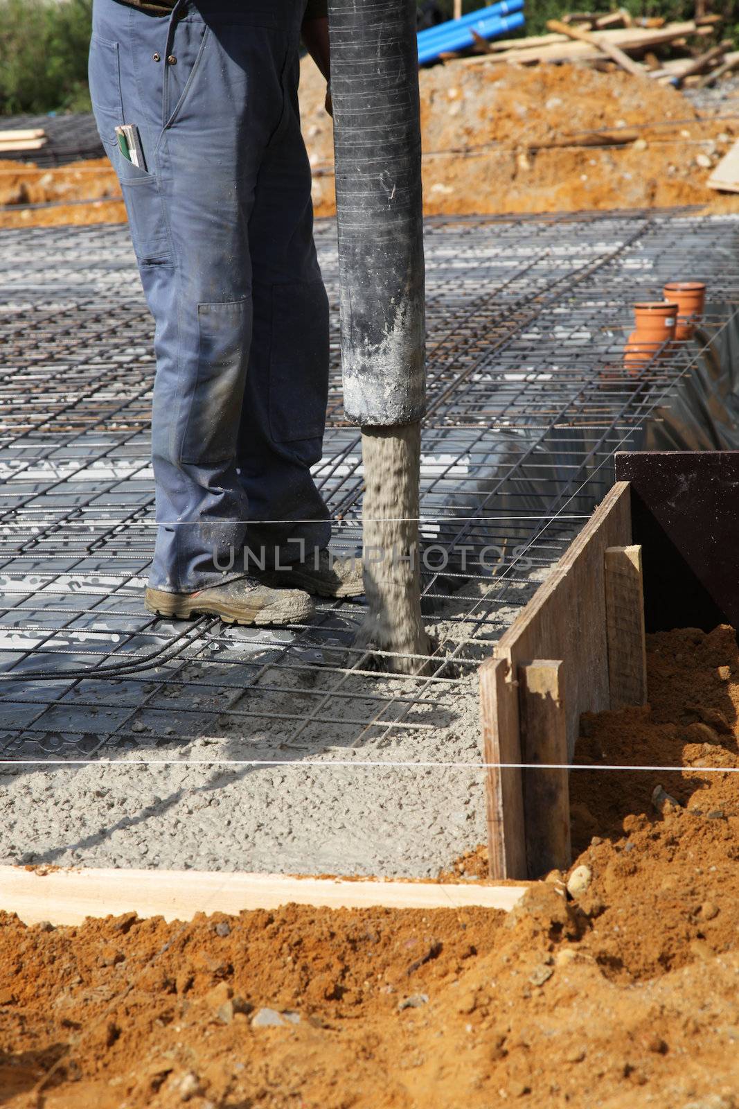 Builder pouring concrete foundations for a new build home over steel reinforing rods from a tube being suspended from a mechanical arm 