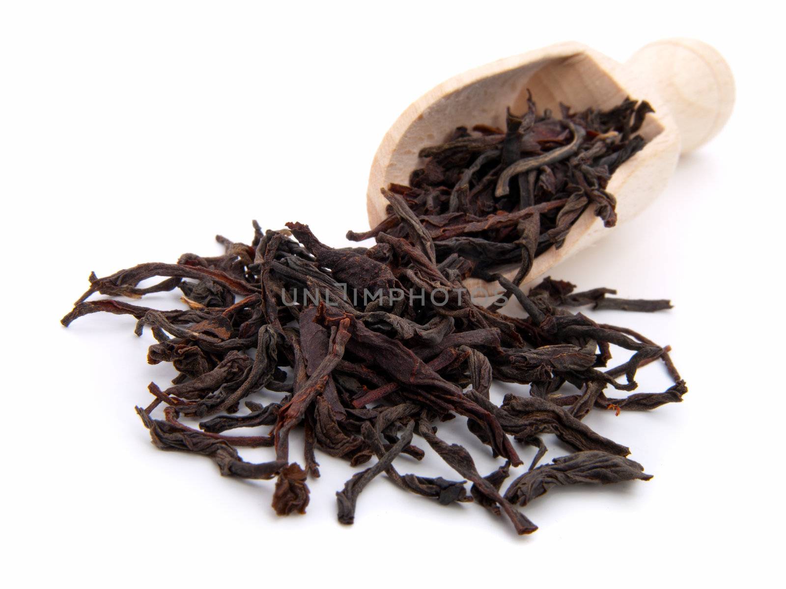 dry black tea leaves on the wooden spoon, on white background