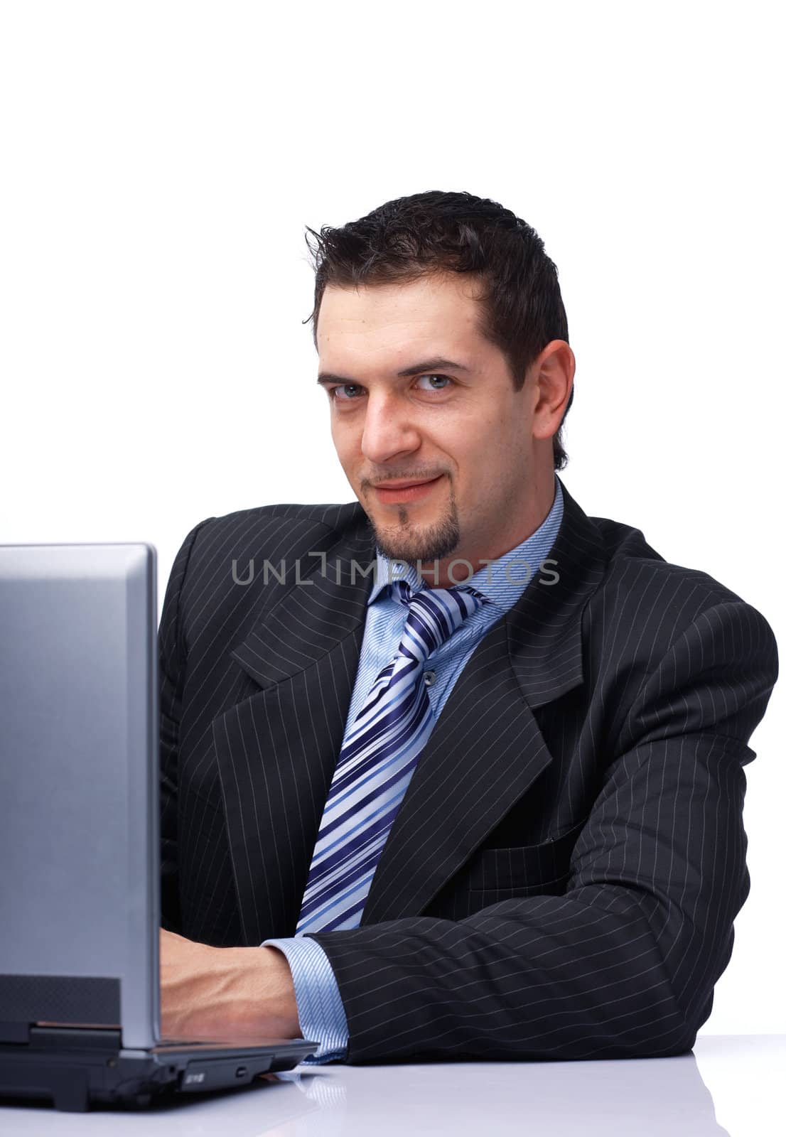 Happy young businessman working on laptop, looking at you over white.