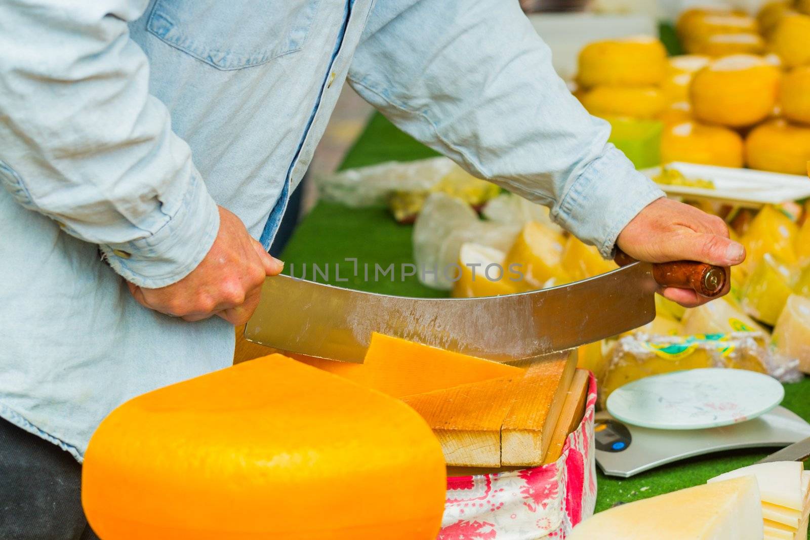 Male hands cutting dutch cheese at the market in Alkmaar