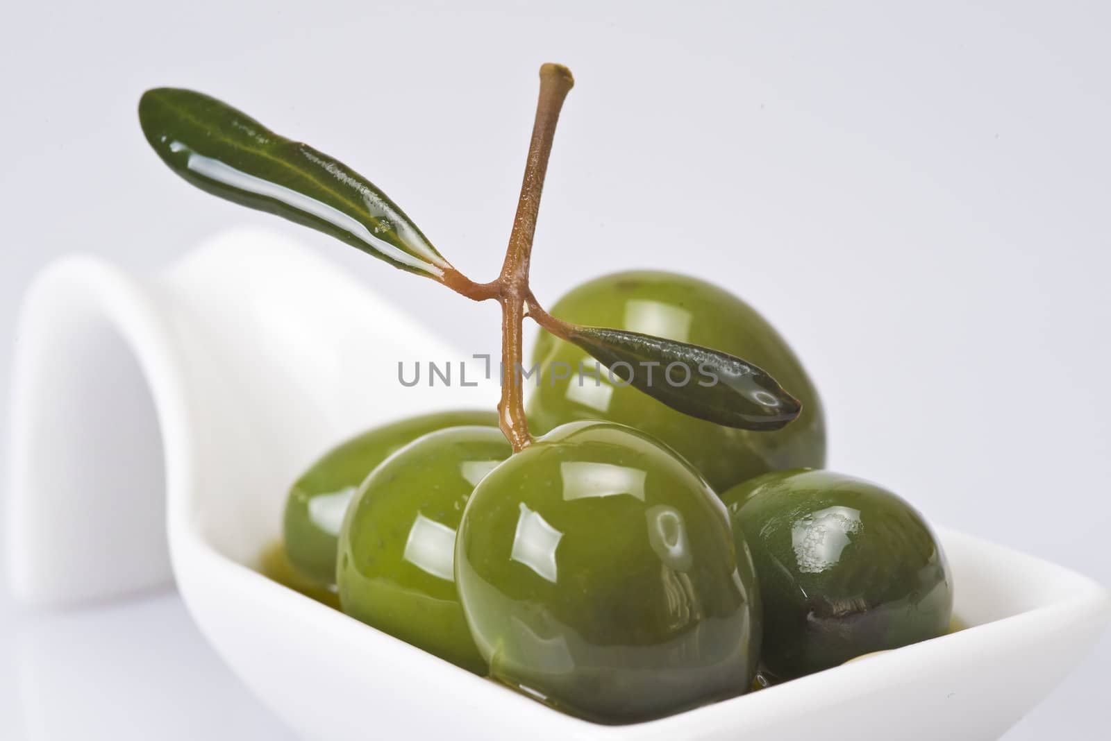 Green olives in a china spoon over a white background
