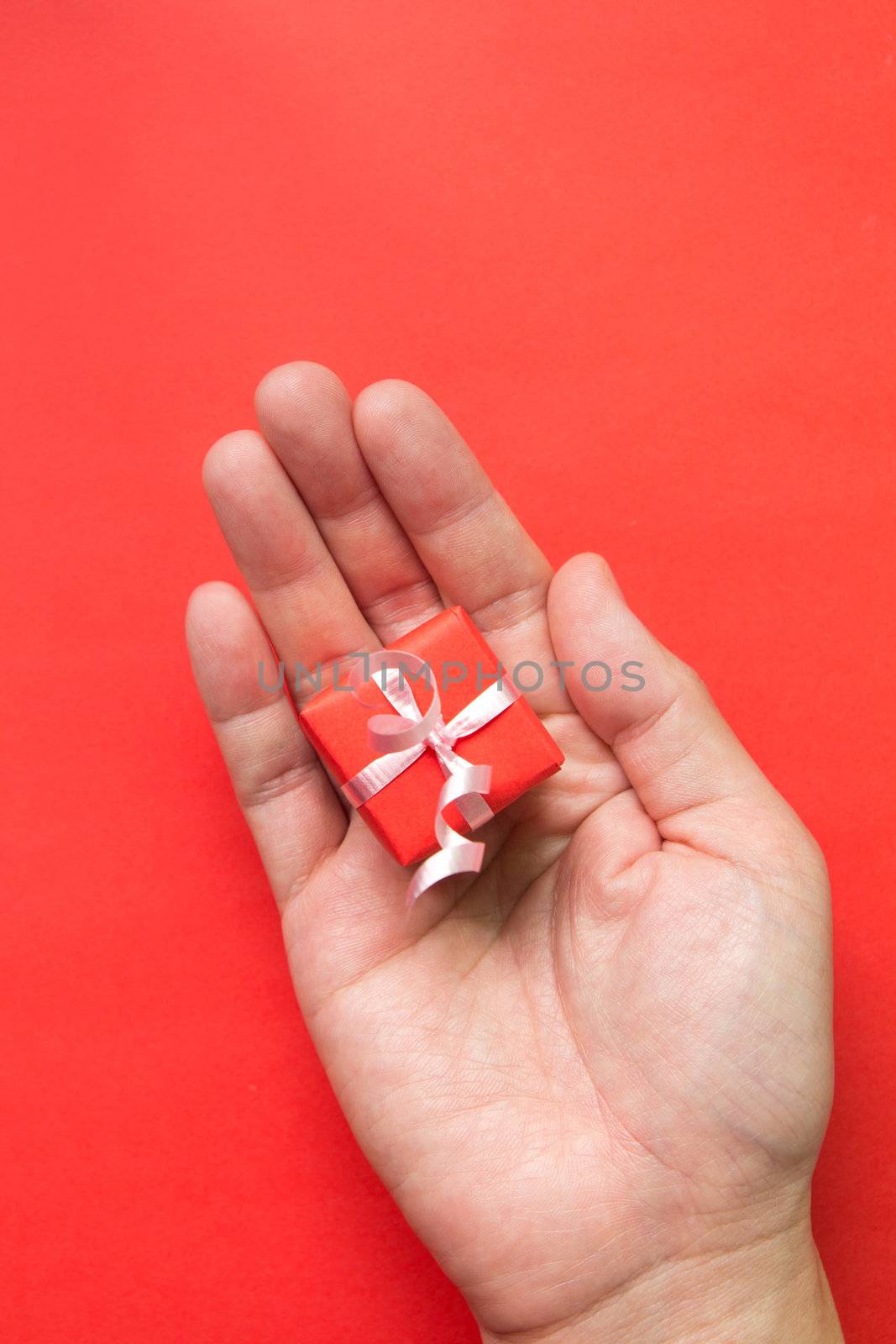 Red gift box with ribbon in hand isolated in red background