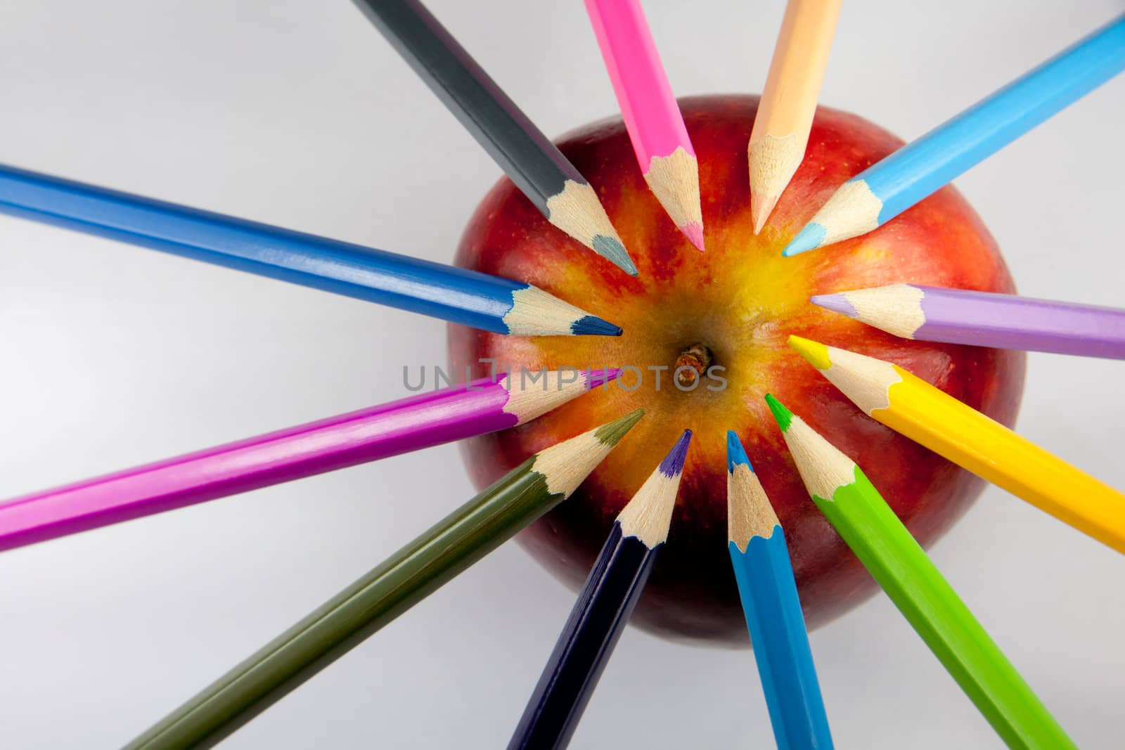 Color pencils forming a circle with their tips on a red and yellow apple against a white background.