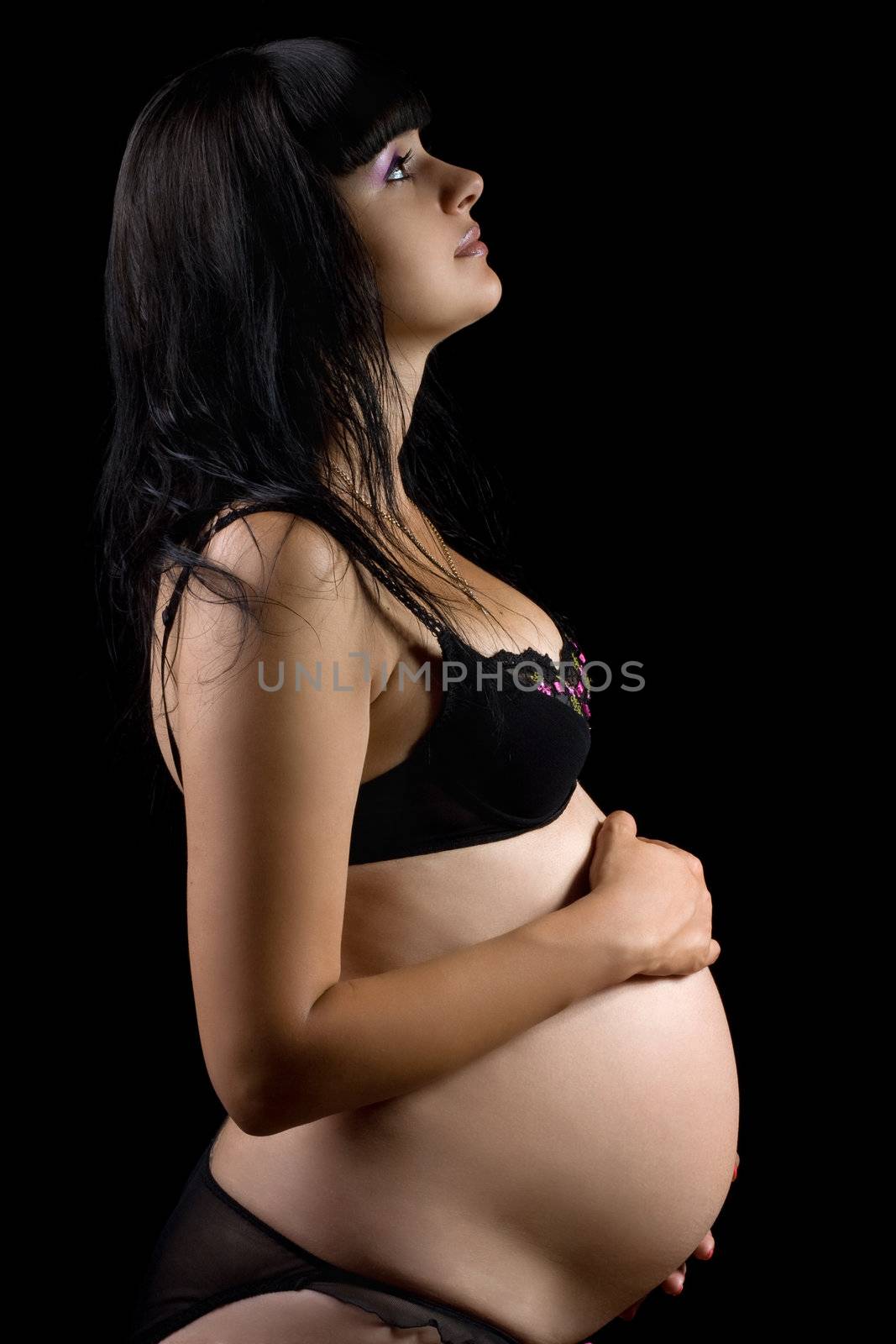 Pregnant young brunette in lingerie. Isolated on black