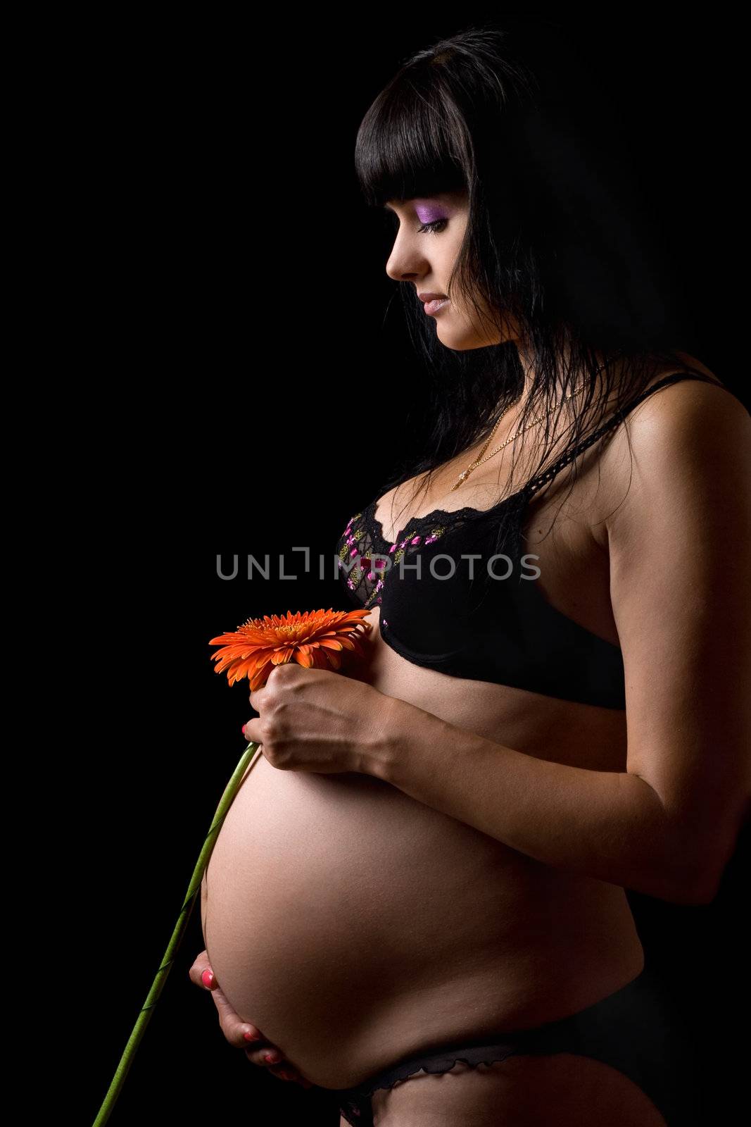 Pregnant young brunette with red flower. Isolated on black