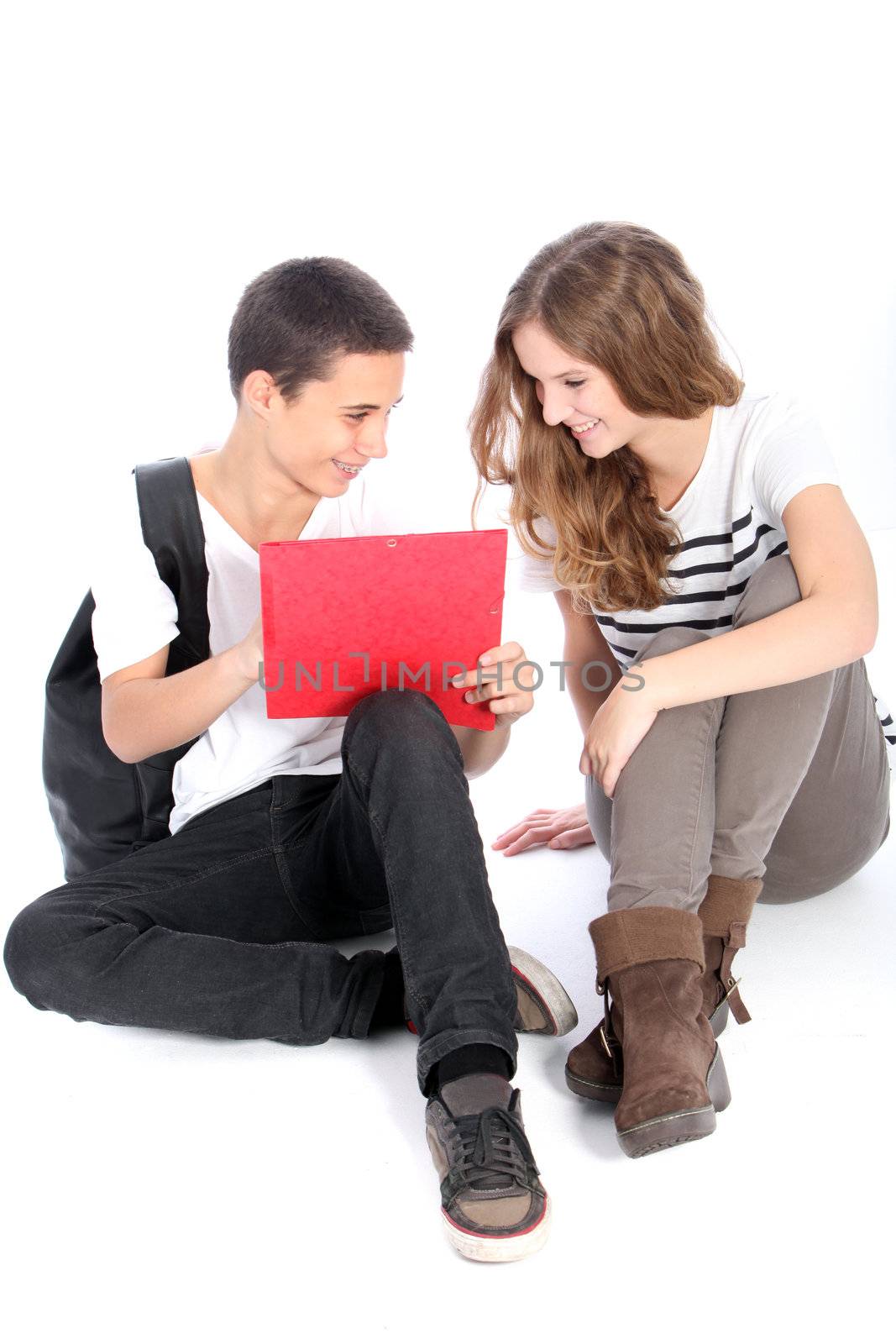 Two happy trendy young teenage students sitting together on the floor working on a project isolated on white