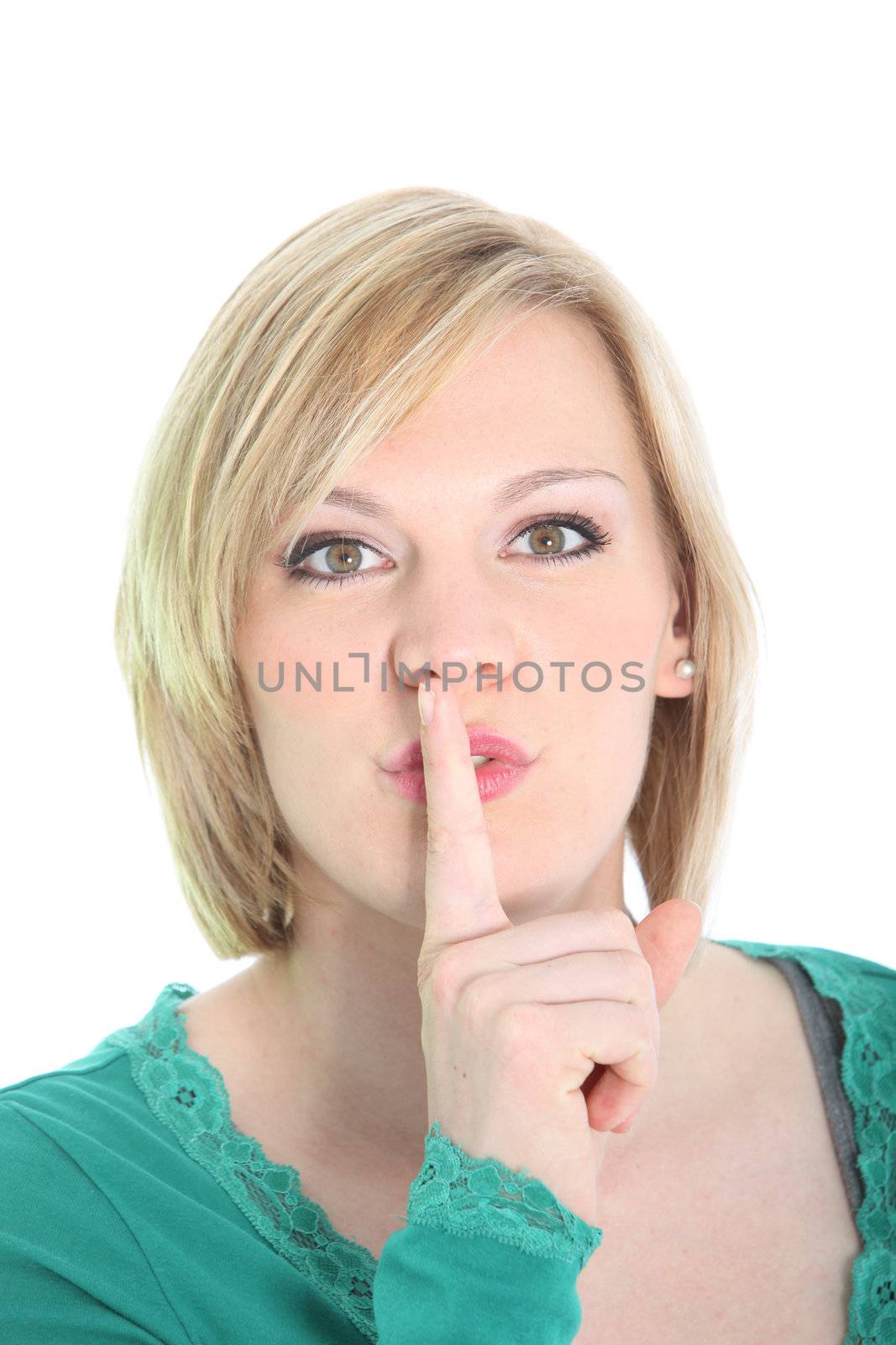 Attractive young blonde woman requesting quiet with a hushing gesture raising her finger to her lips isolated on white