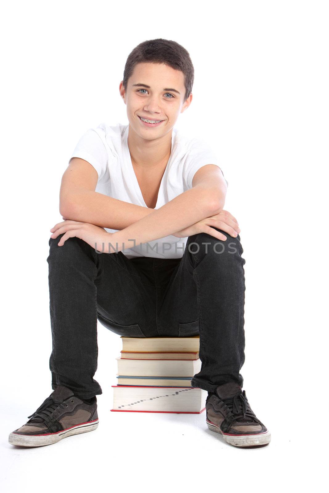 Smiling teenager sitting on pile of books isolated on white