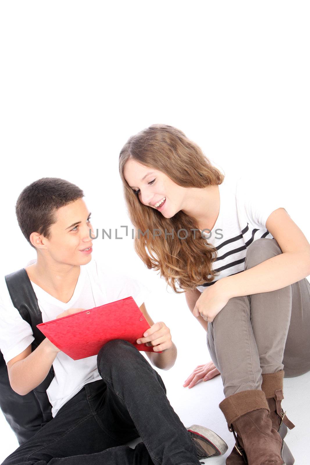 Two younfg teenage students sitting on the floor laughing together at something that the boy is displaying in his college folder isolated on white