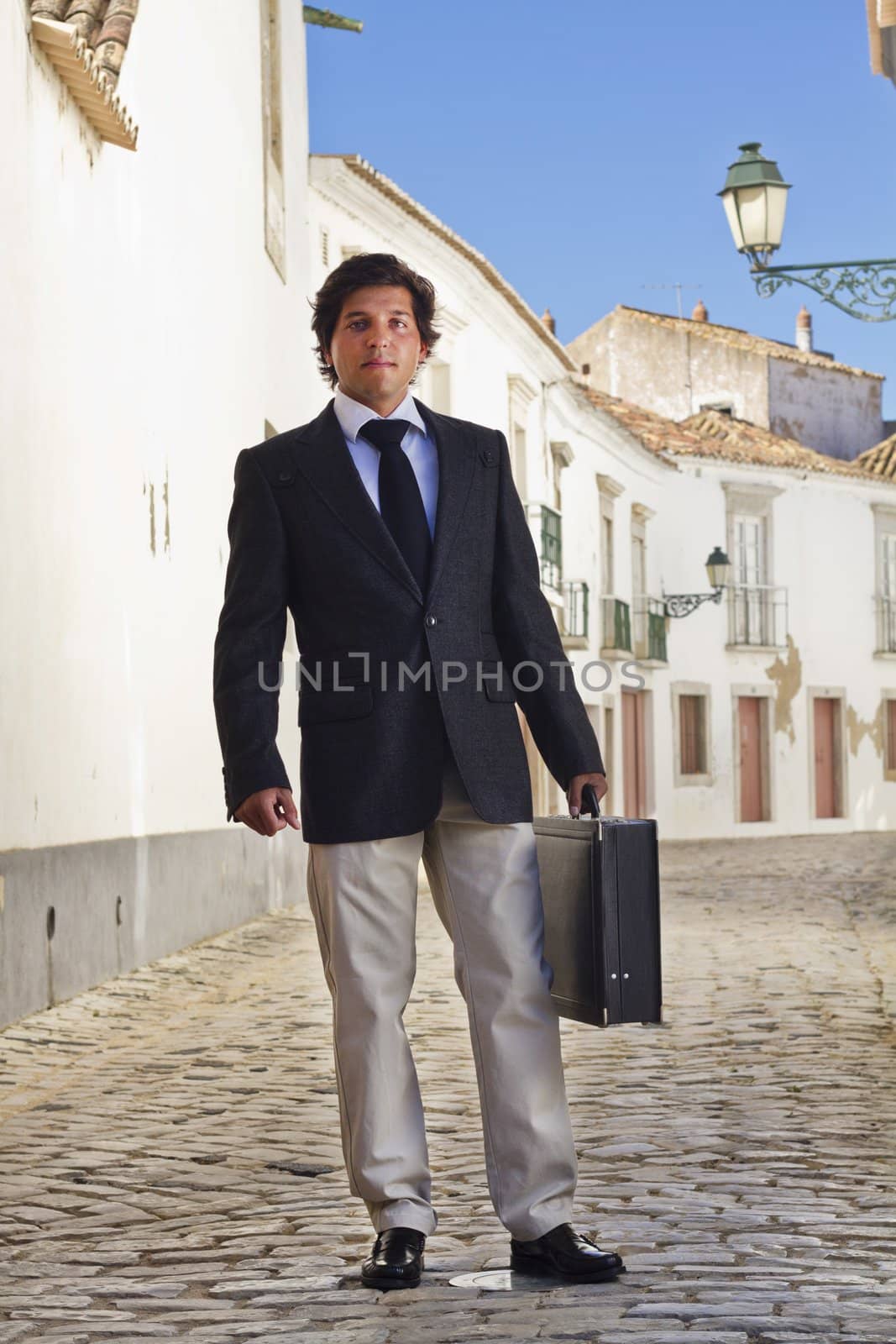 View of a happy business man with a black suitcase on a European city.