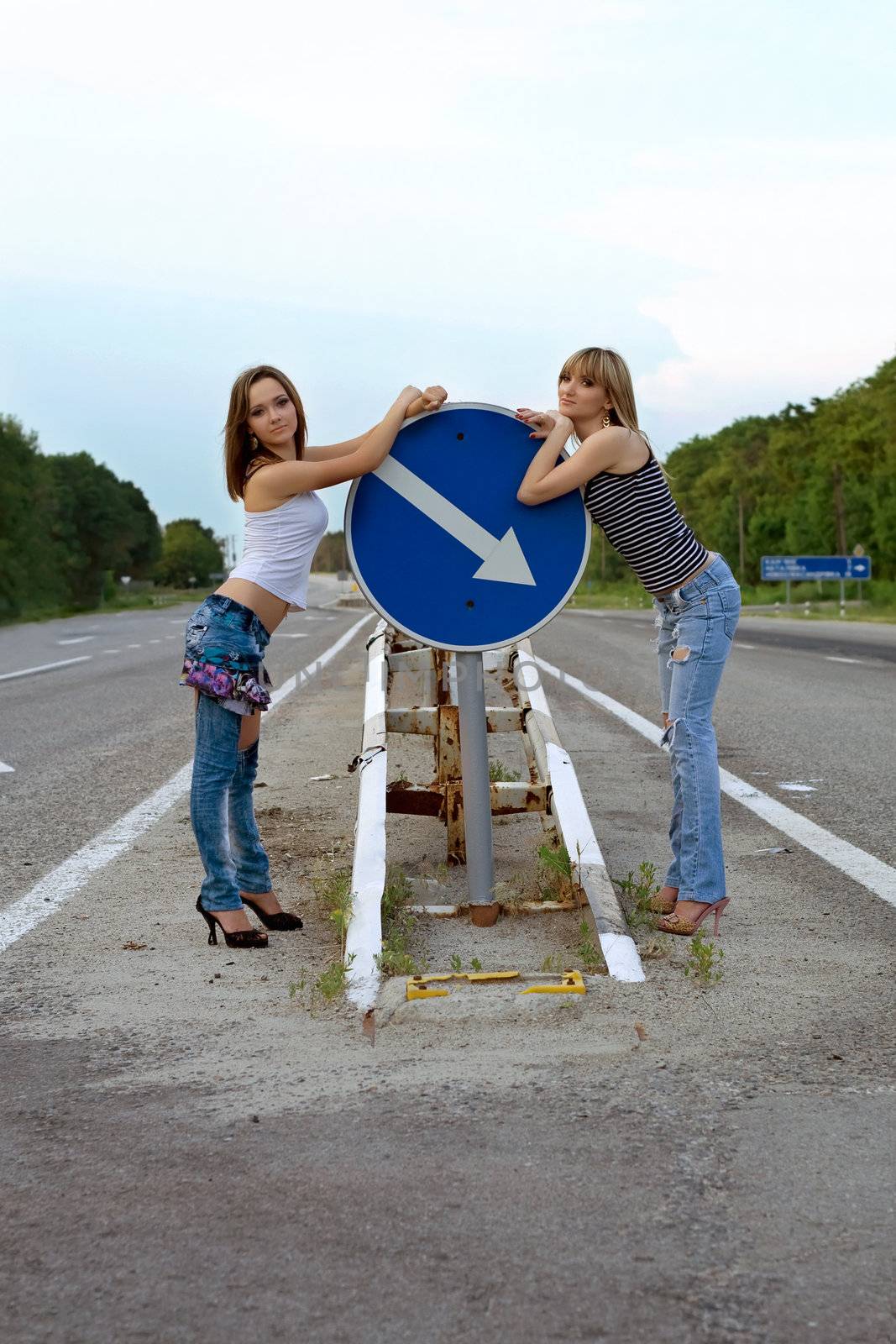 Two pretty girls stand on a road near the sign