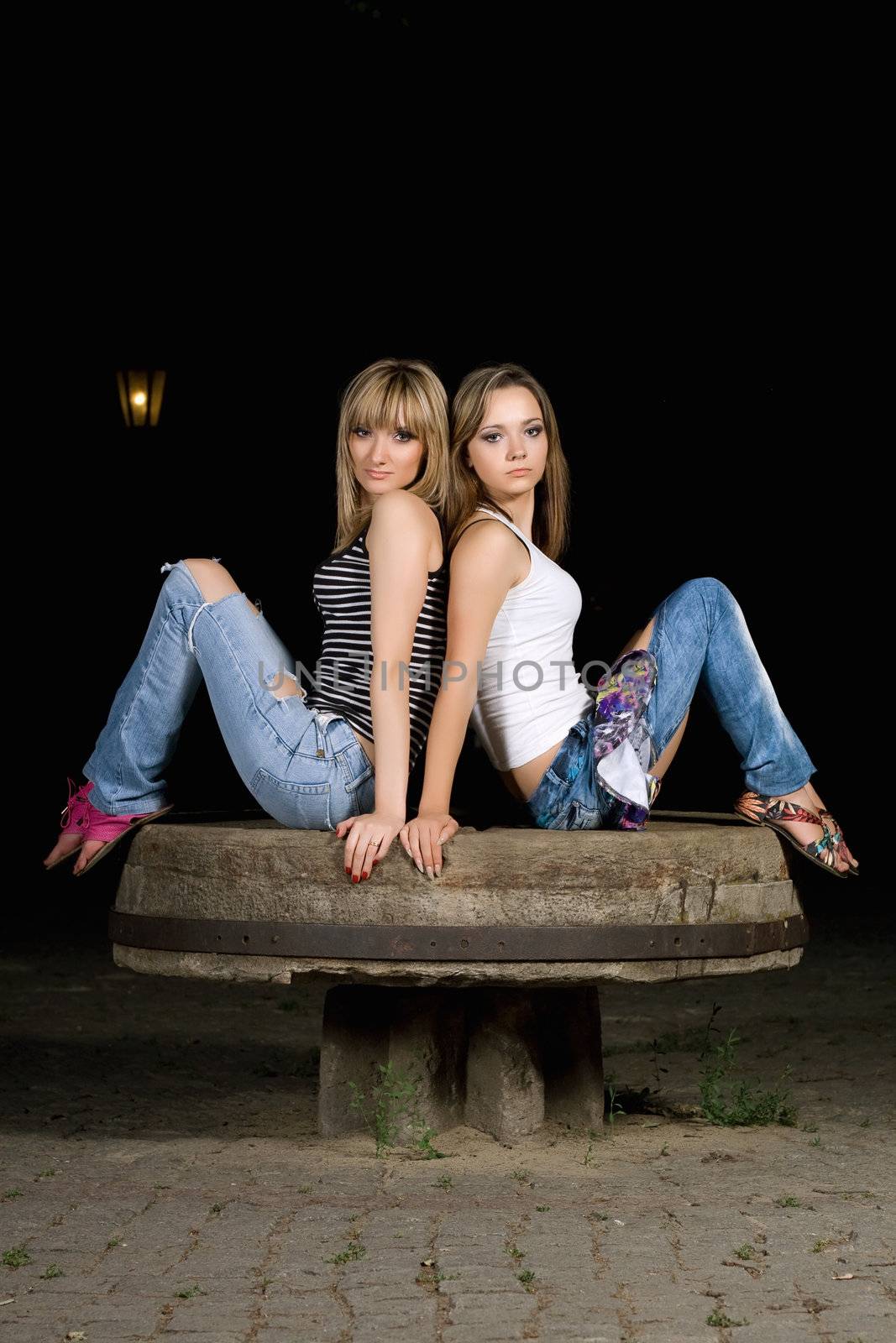 Two attractive girls sitting on a stone bench